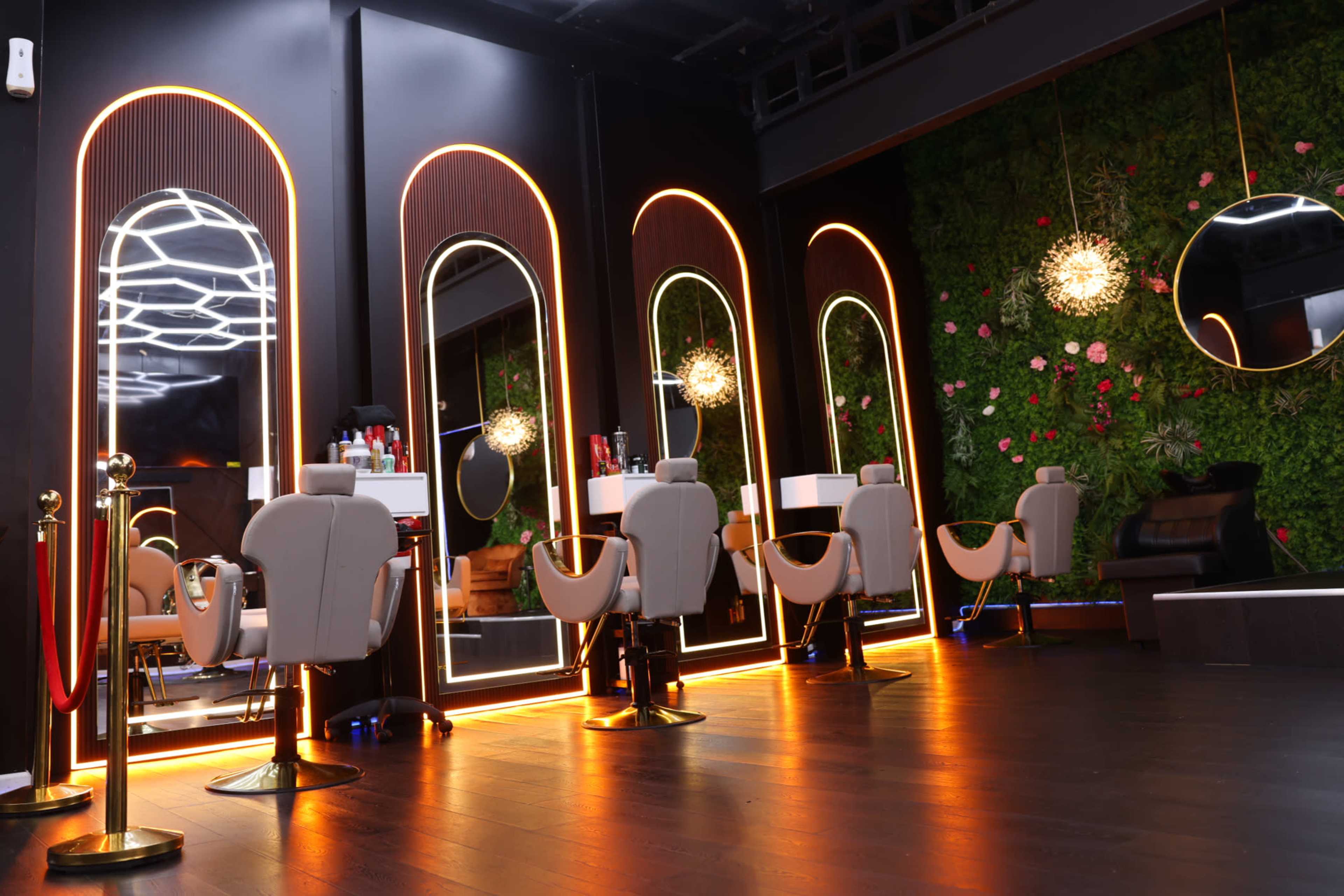 The image shows a modern salon interior with illuminated mirrors, stylish chairs, and a green wall adorned with flowers.