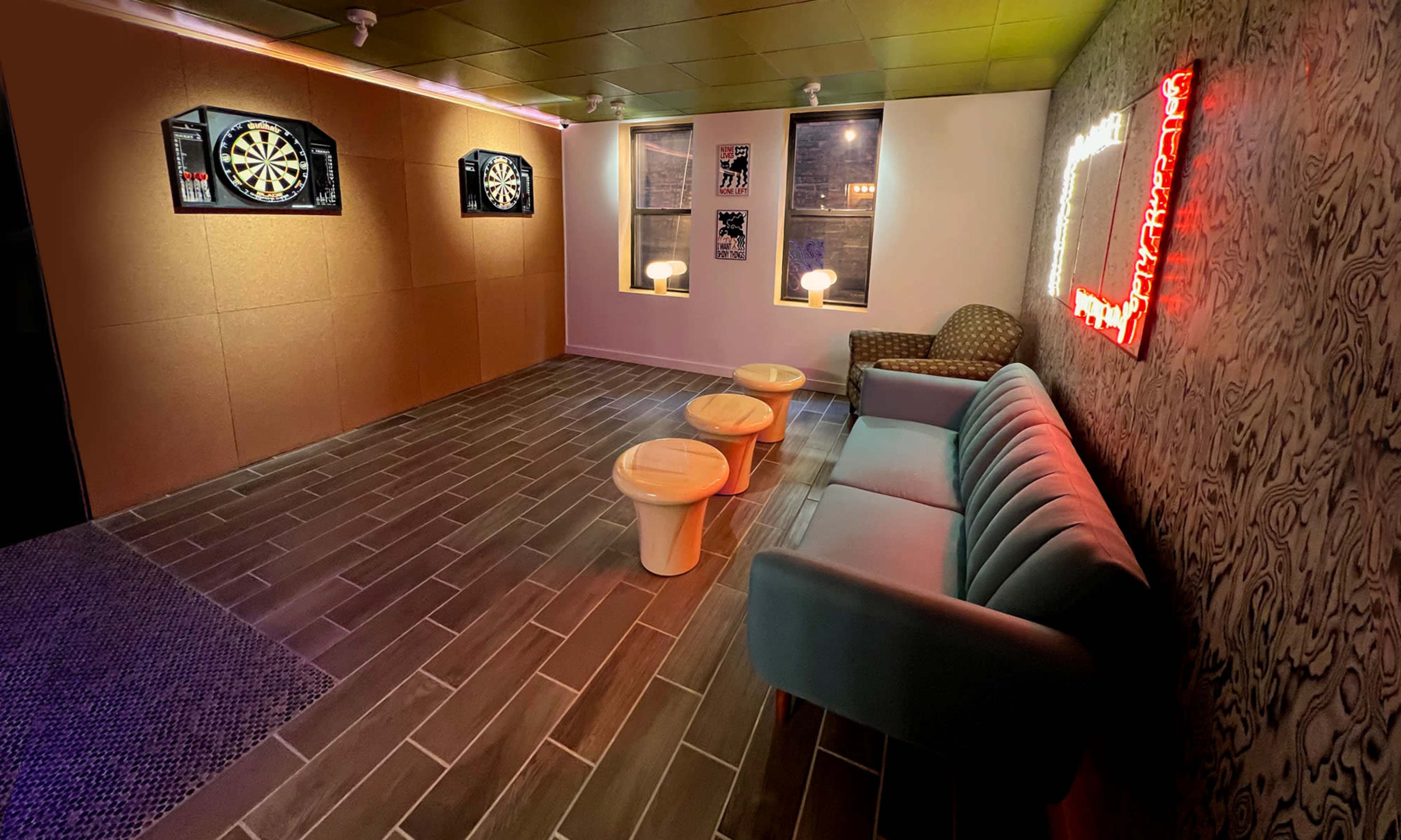 The scene shows a room with two dartboards on the wall, a couch, three small tables, and decorative lighting.