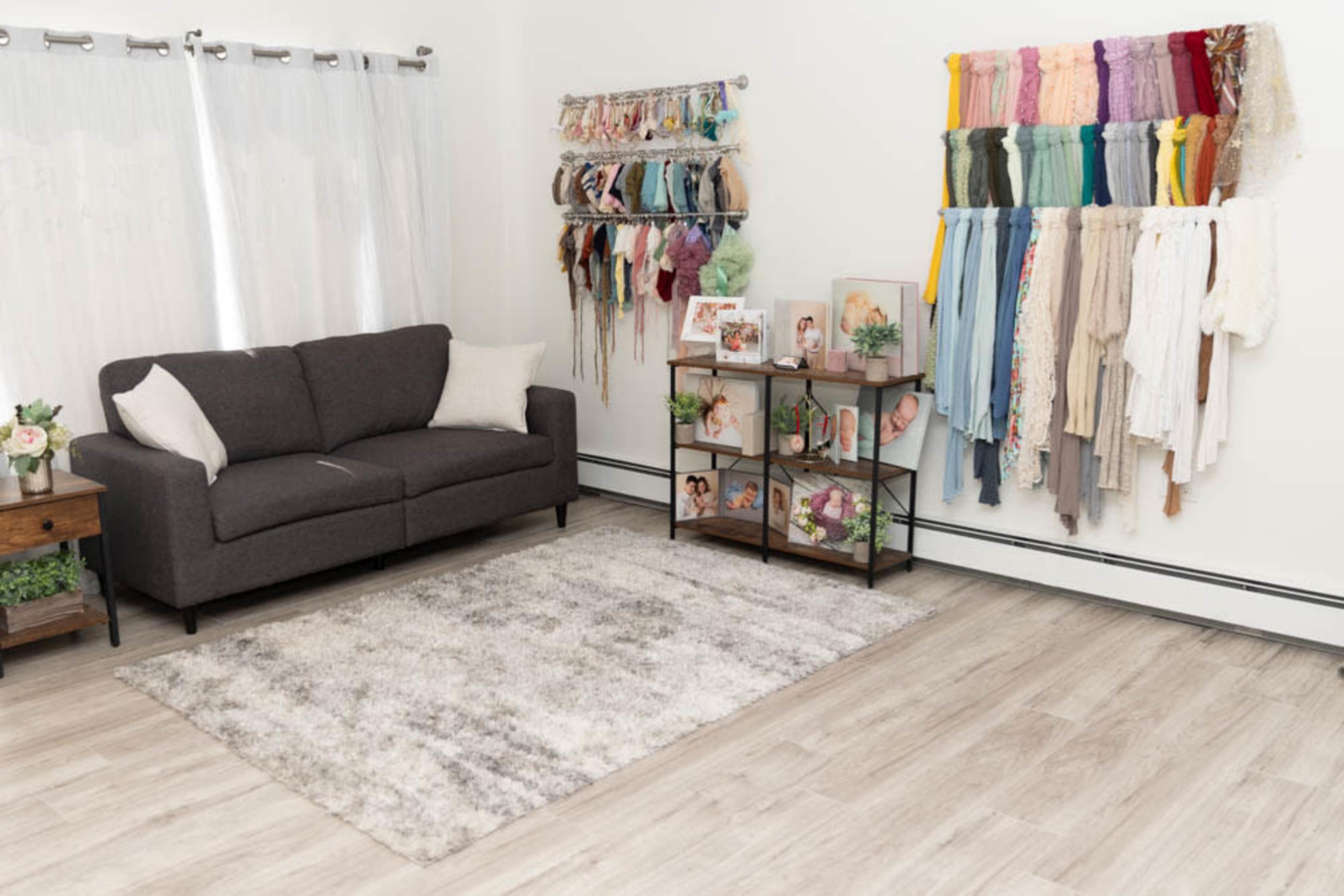 The image shows a living room with a gray sofa, a display of colorful fabric swatches on the wall, and a small shelf featuring framed photos and decorative items.