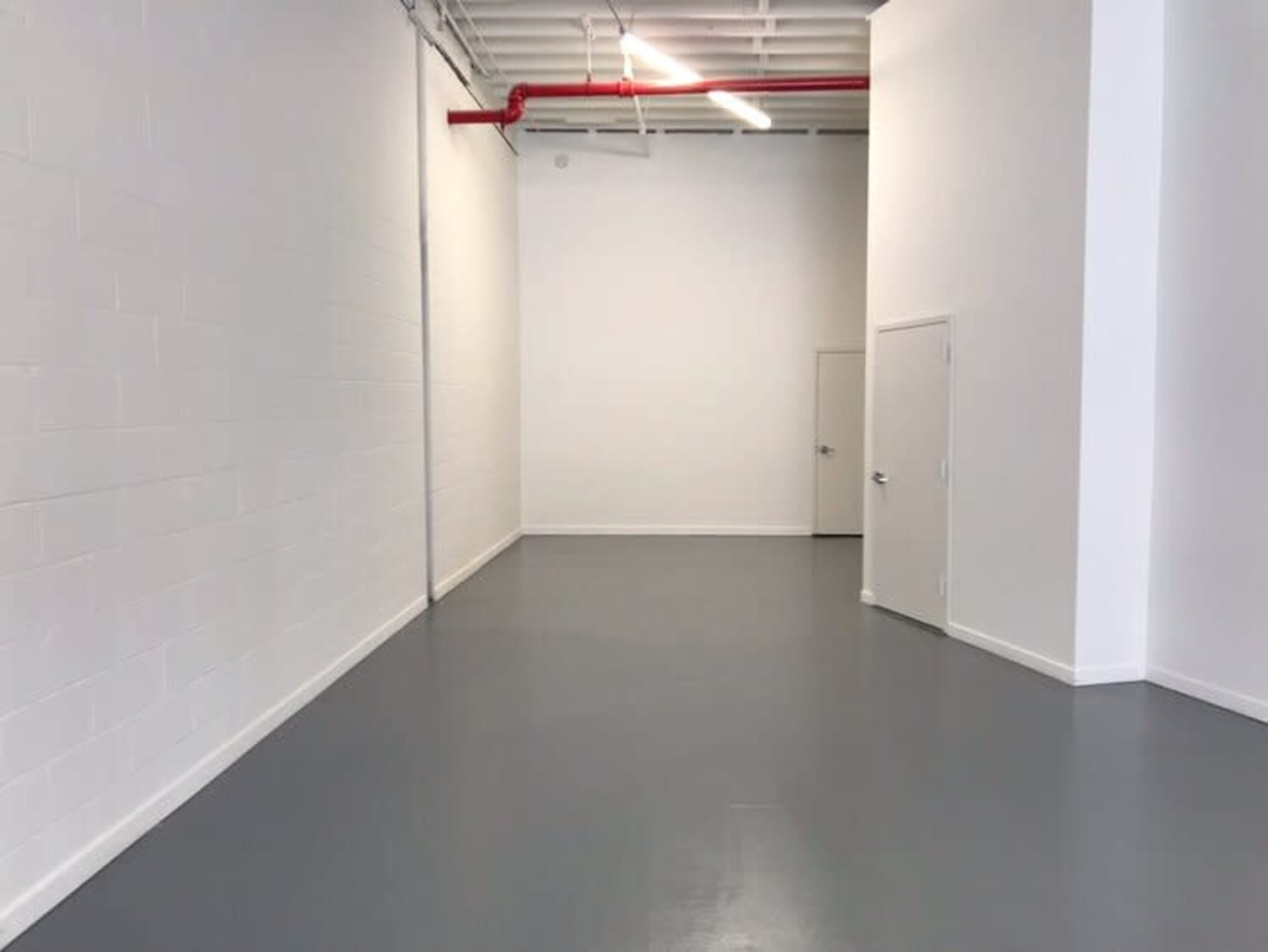 An empty, white-walled room with a gray floor and a single door on one wall.