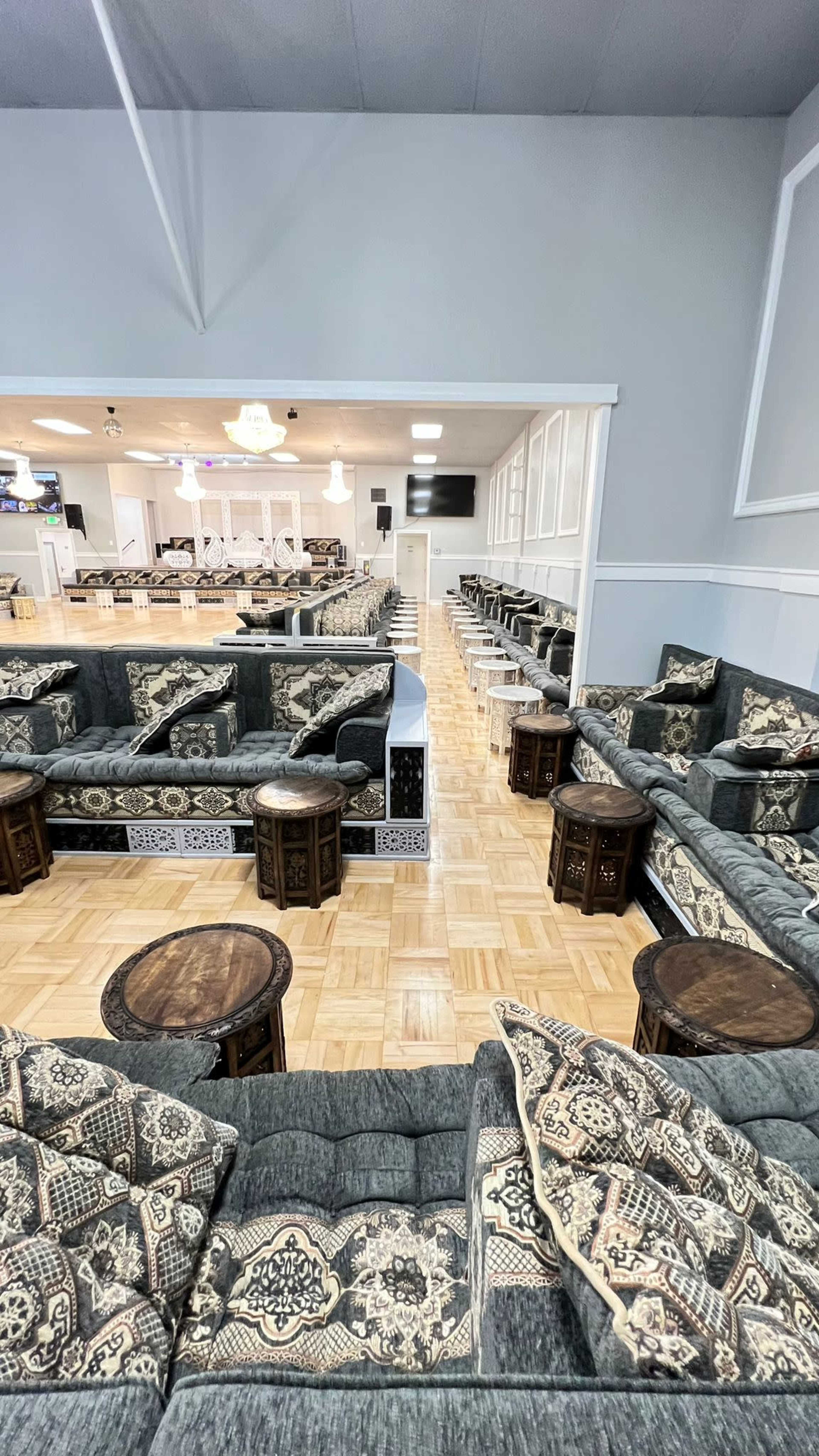 The image shows a spacious lounge area furnished with patterned couches and small wooden tables arranged around a wooden floor.