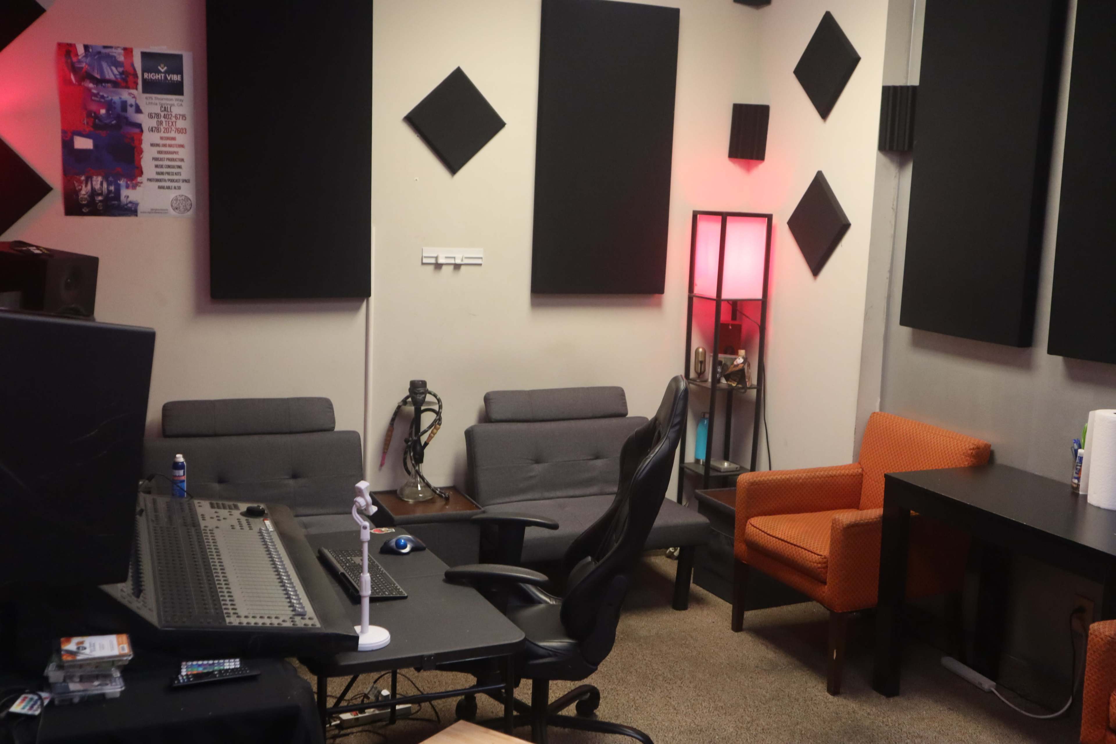 A music studio with a mixing console, two gray sofas, an orange chair, and soundproofing panels on the walls.