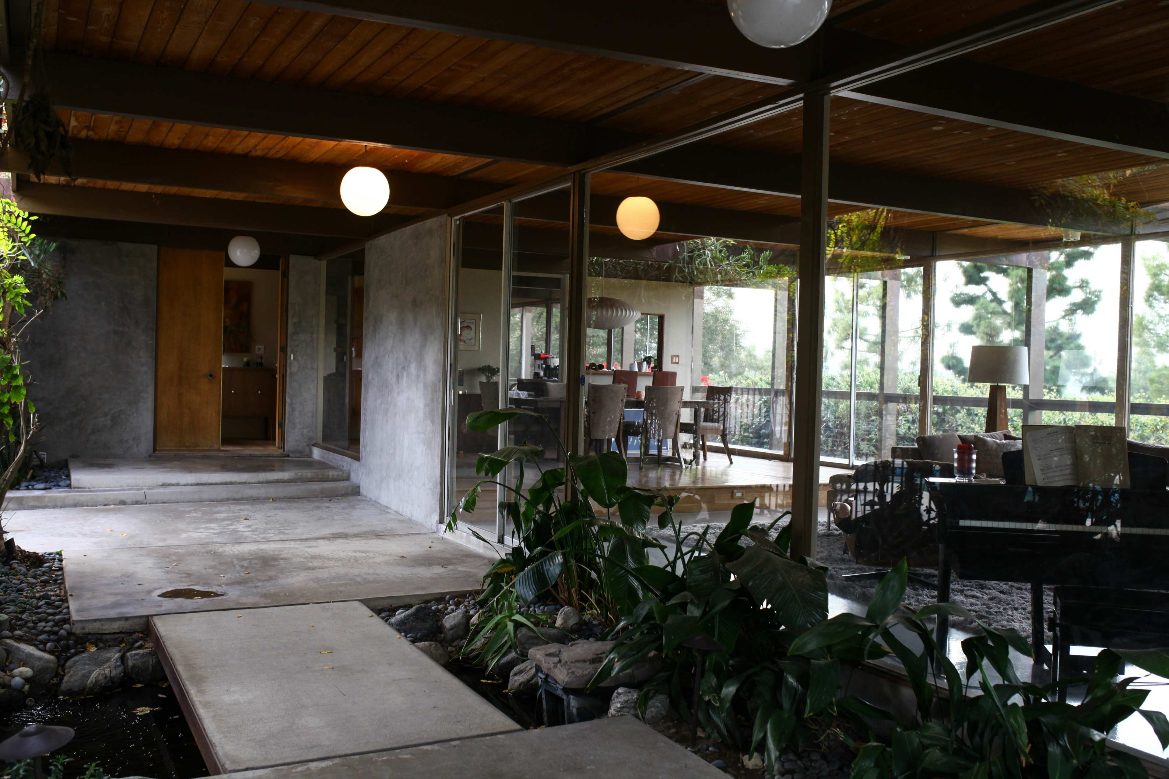 A modern interior space with large glass windows, a concrete and wood structure, and green plants integrated into the design.