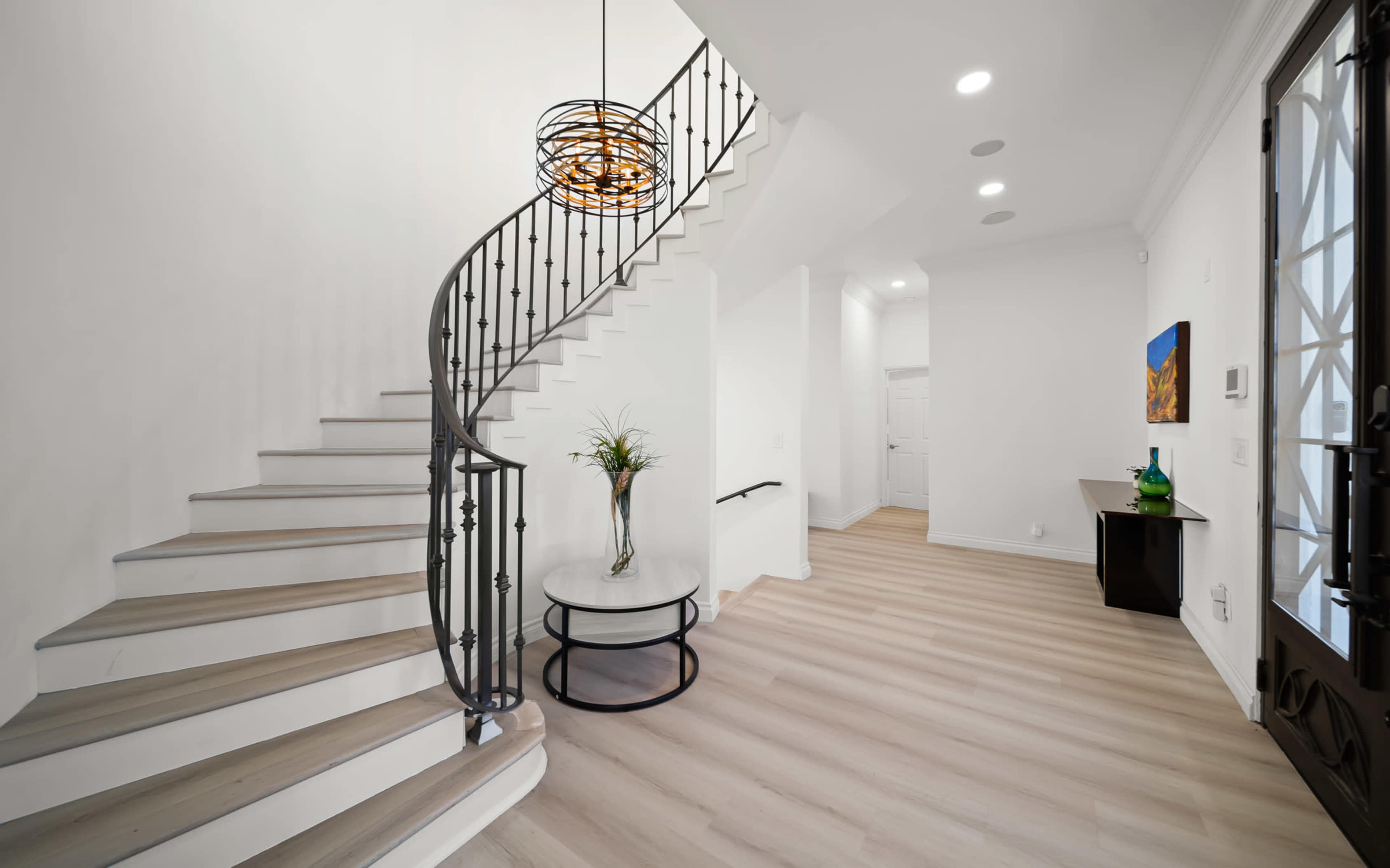 A spiral staircase leads to an upper level in a bright entryway featuring a round table and decorative elements.