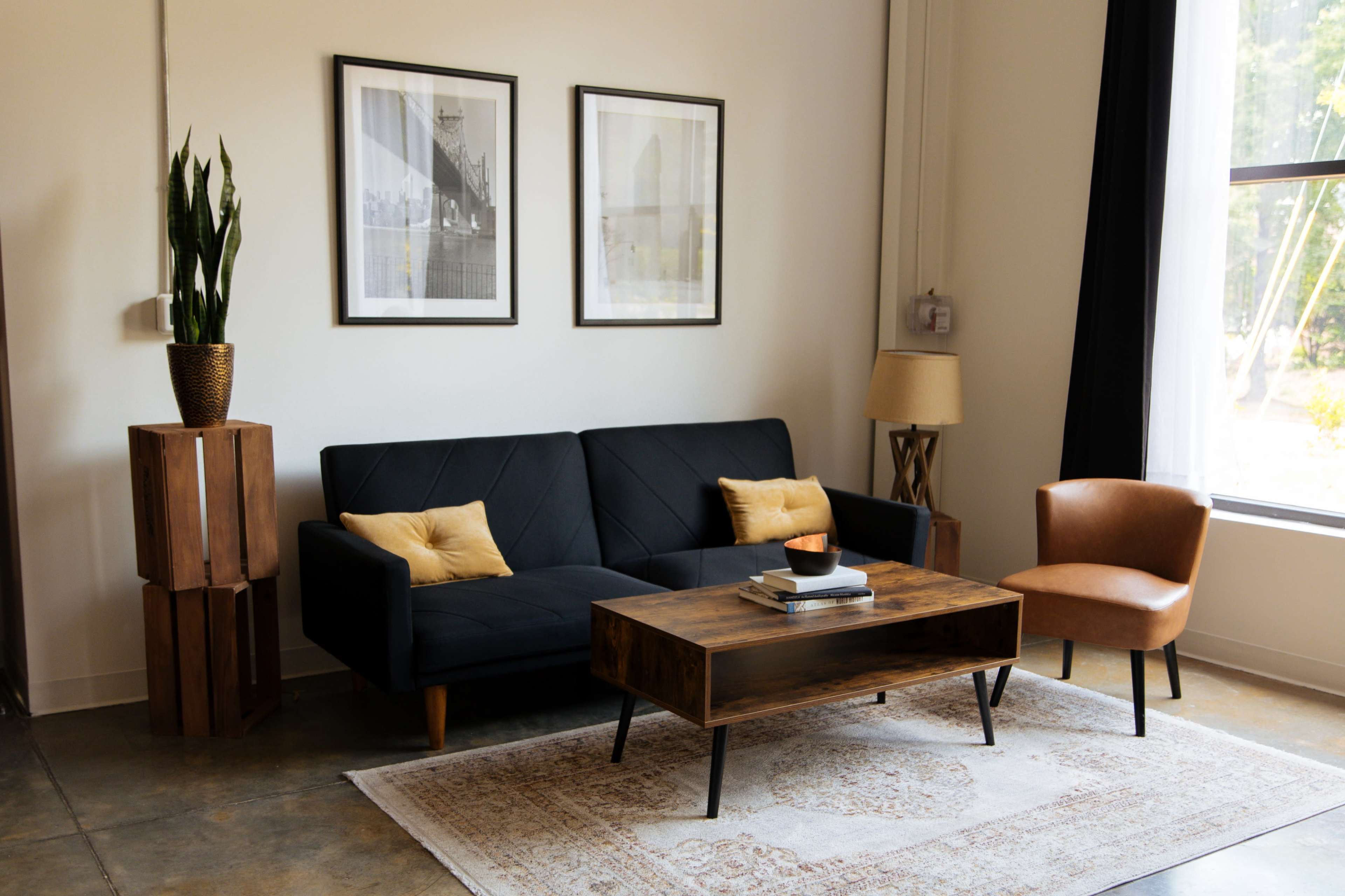 A modern living room featuring a black sofa with yellow cushions, a wooden coffee table, an orange chair, and two framed prints on the wall.