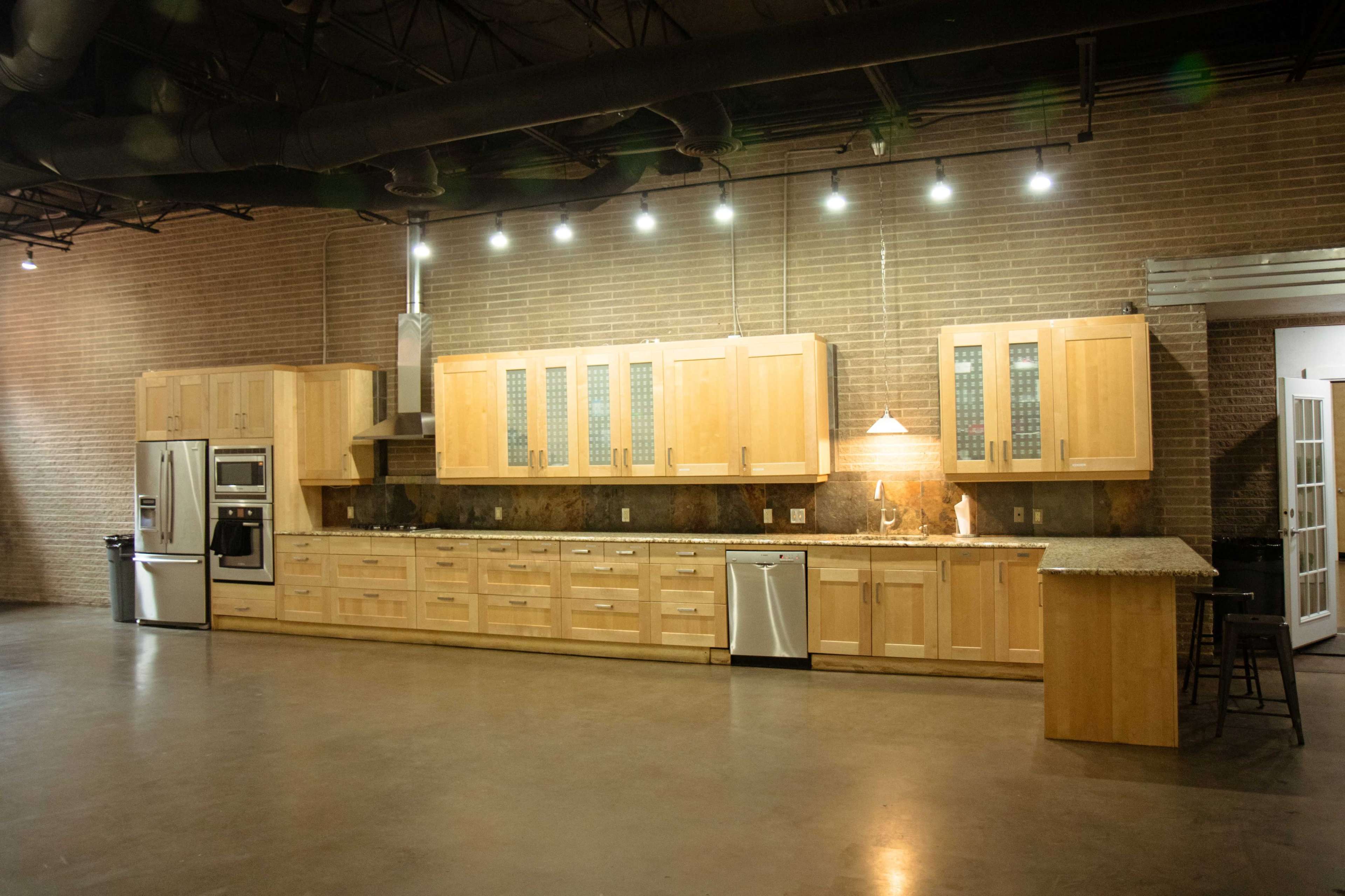 The image shows a spacious kitchen with wooden cabinetry, a granite countertop, and stainless steel appliances, set against a brick wall.