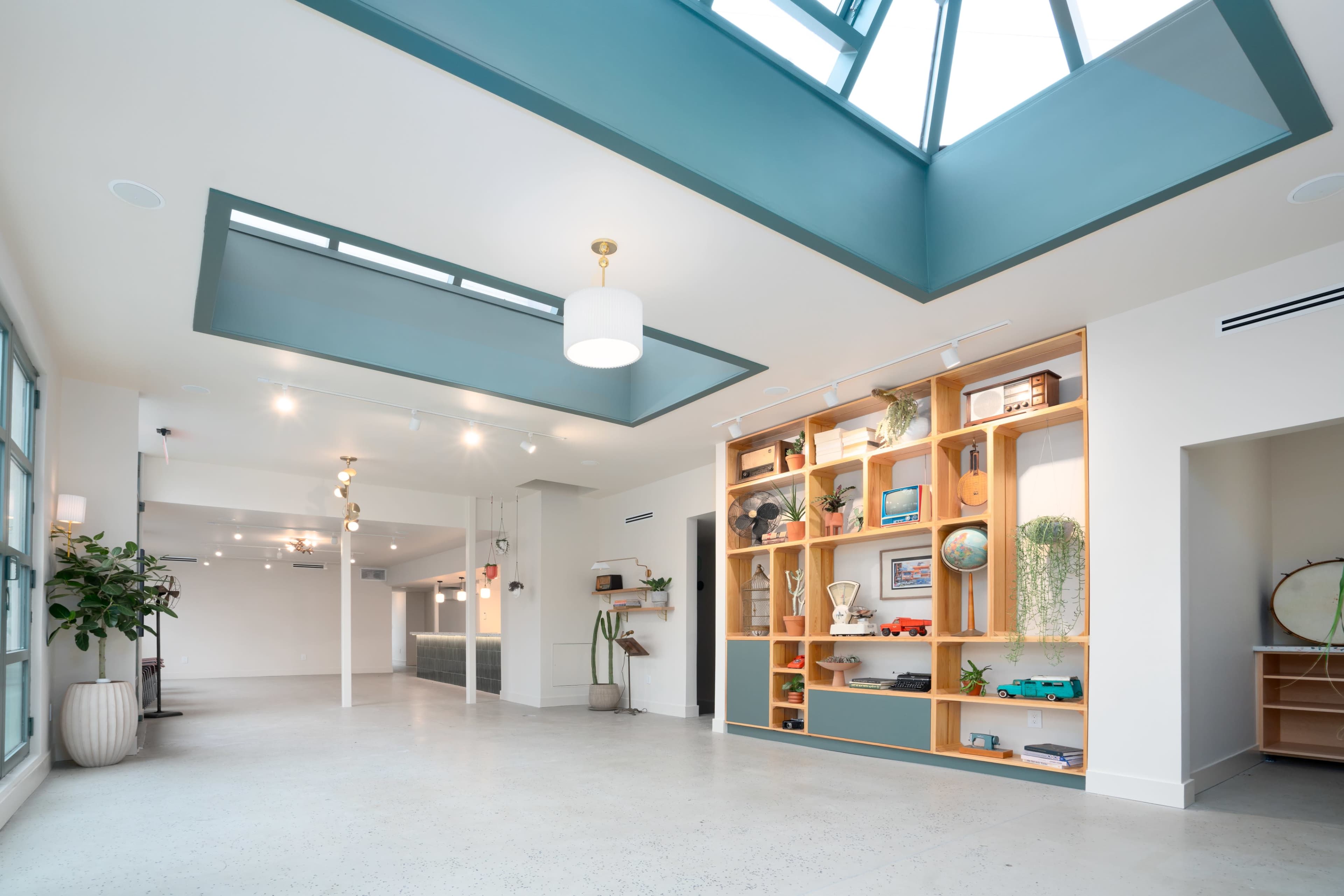A spacious, modern interior with a skylight, a wooden shelf displaying decor items, and polished concrete flooring.
