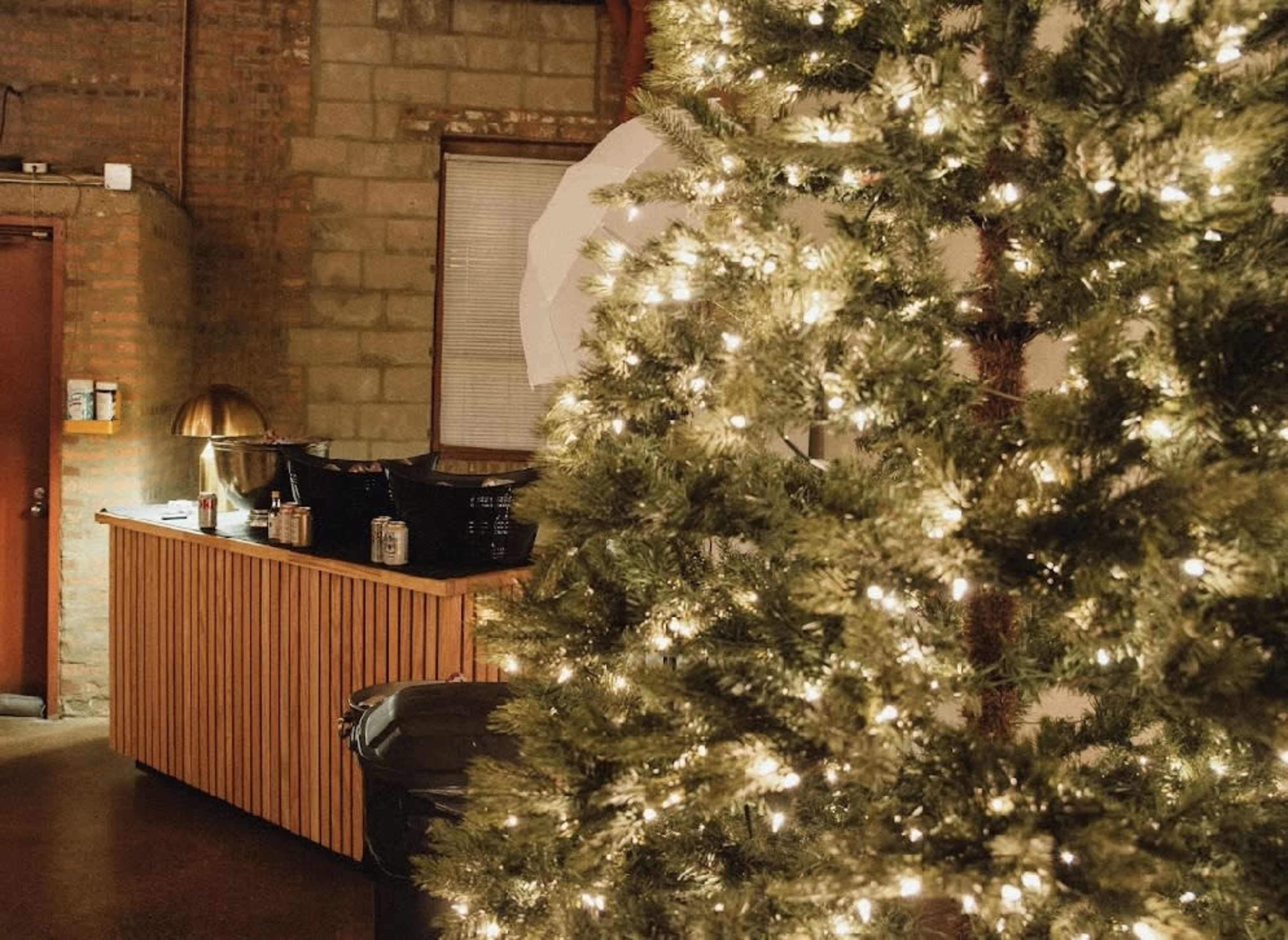 A dimly lit interior space with a decorated Christmas tree on the left and a wooden counter with a lamp and baskets in the background.