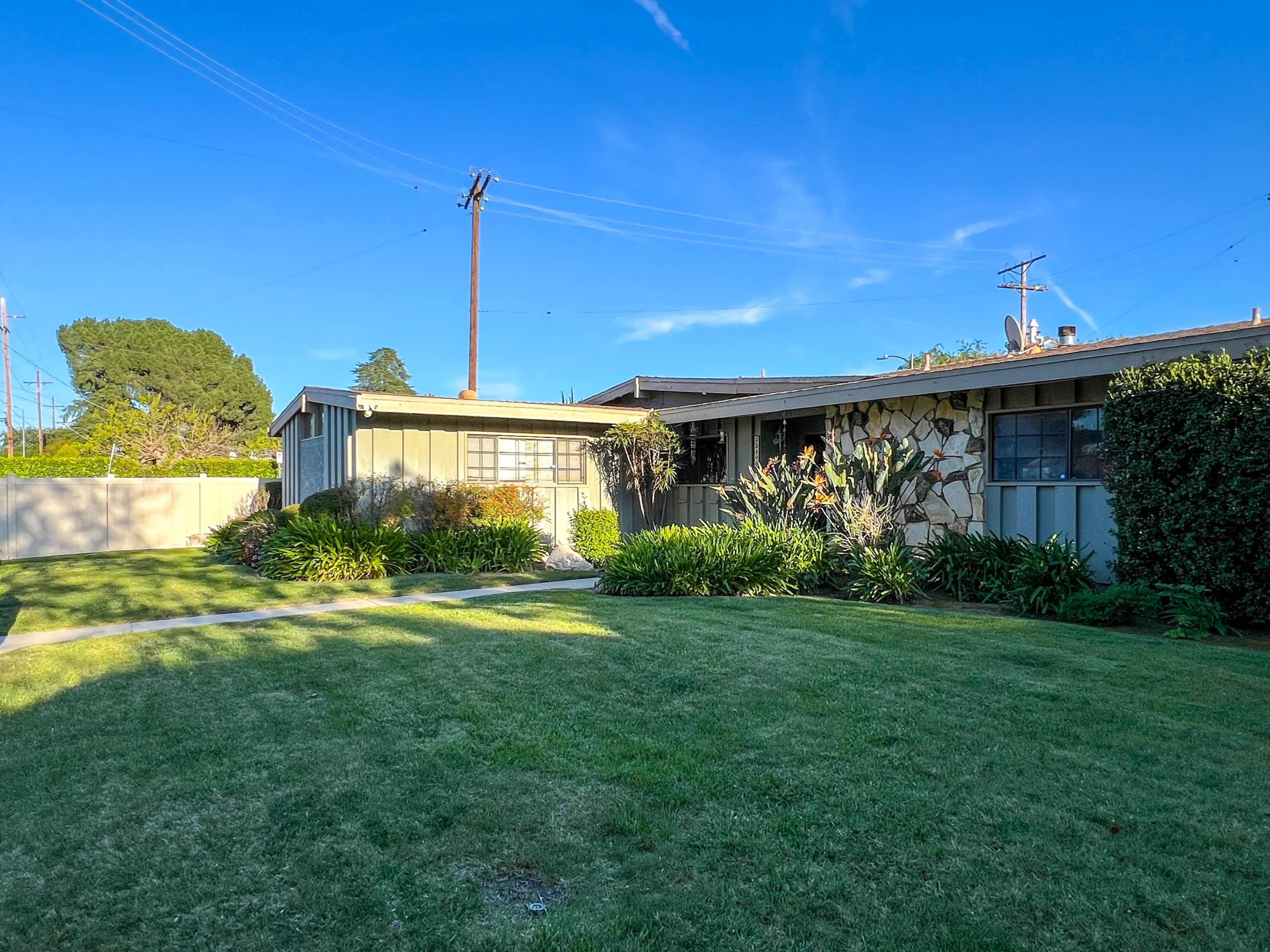 The image shows a single-story house with a stone facade and landscaped front yard, situated under a clear blue sky.