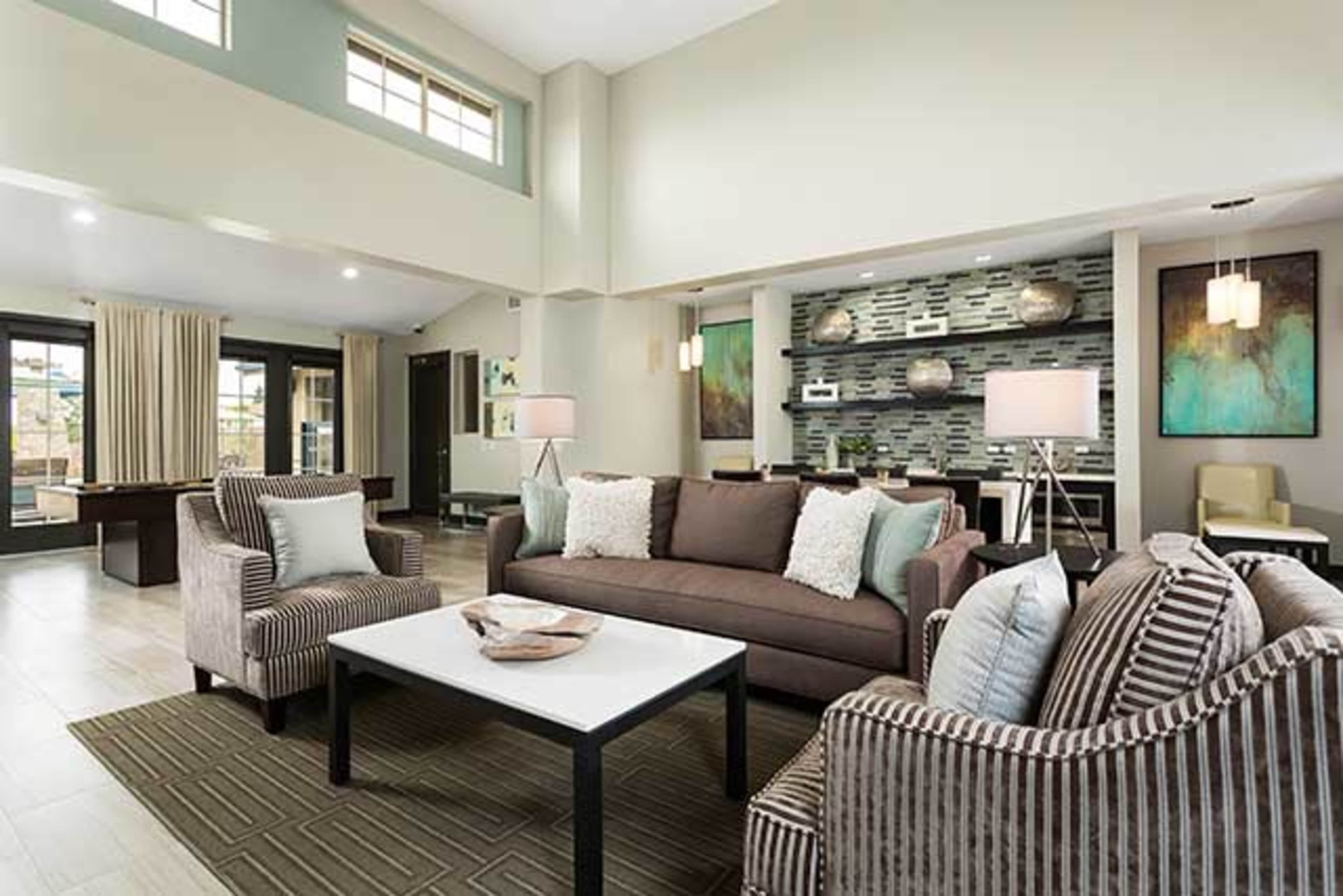 A modern living area featuring a brown sofa, patterned armchairs, a coffee table, and a decorative wall with artwork.