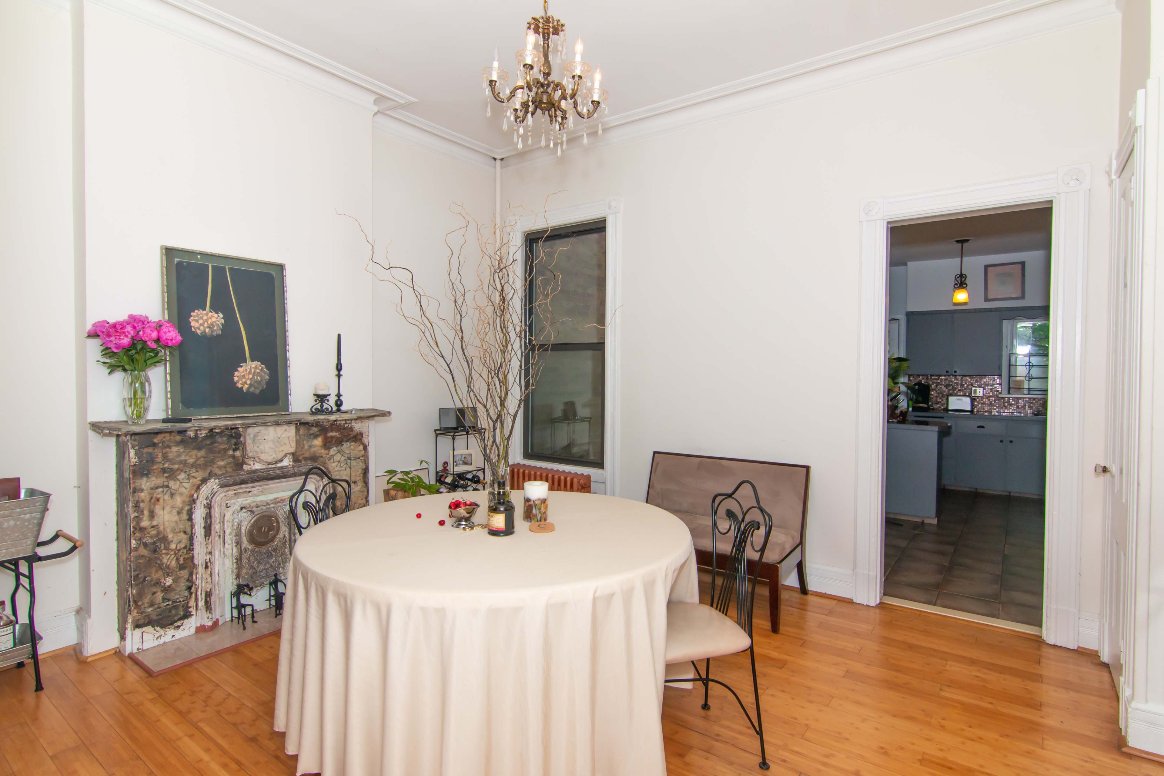 A dining area featuring a round table with a light-colored tablecloth, surrounded by two chairs, and a decorative fireplace adorned with flowers and branches.