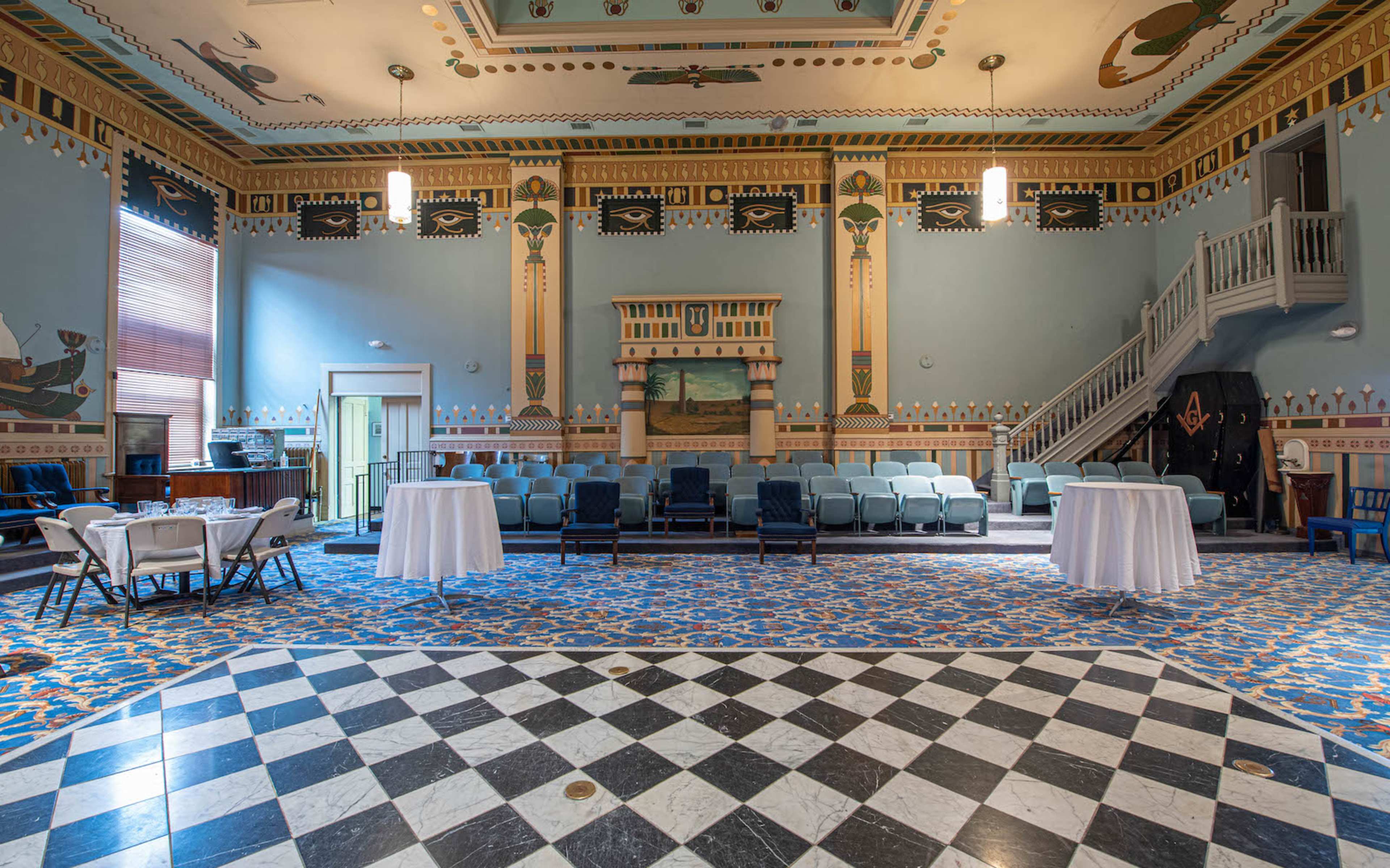 A spacious room with a patterned tile floor, arranged seating, and decorative murals on the walls and ceiling.