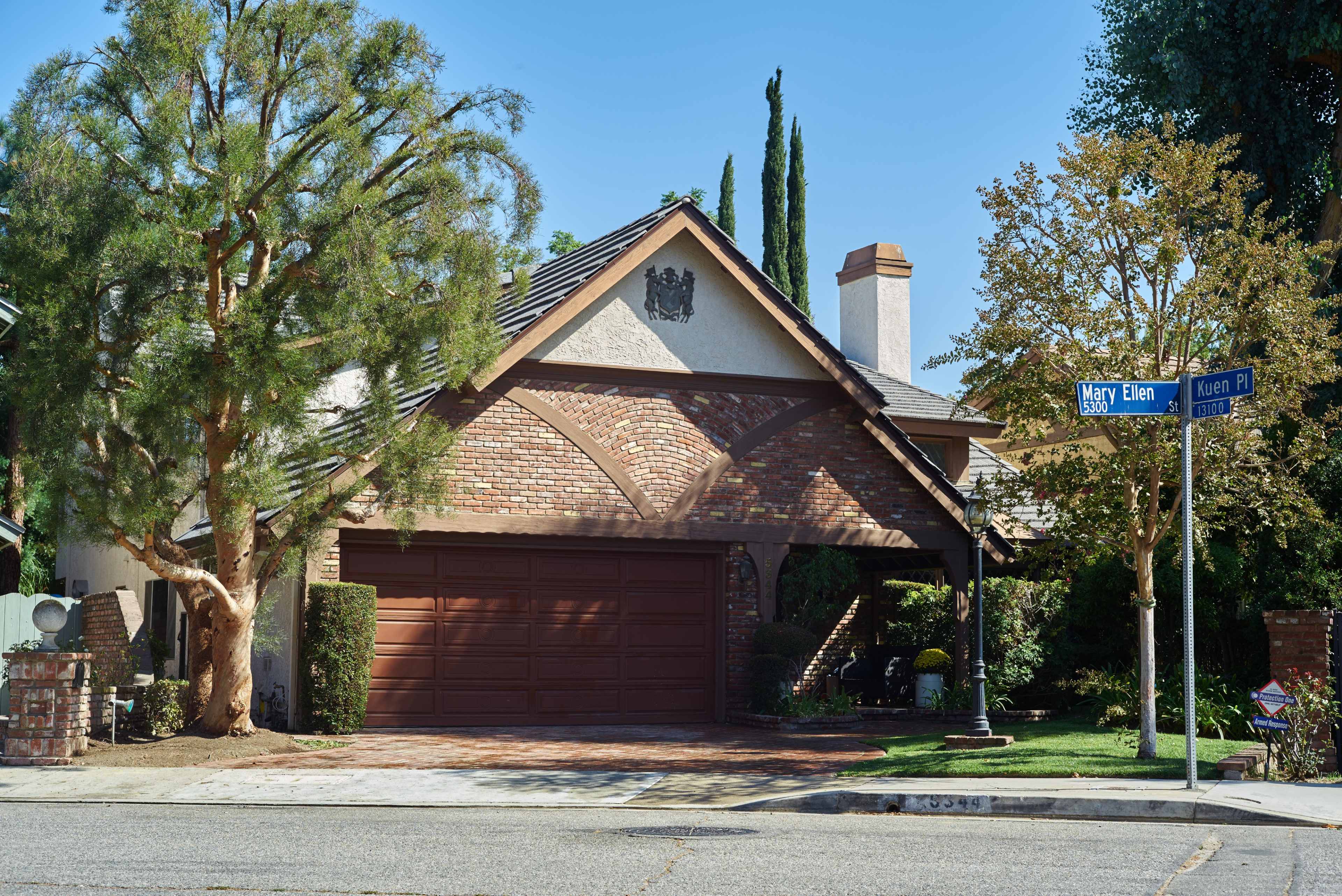 A residential home with a brick facade and a two-car garage sits at the corner of Mary Ellen and Keren Place, surrounded by trees and landscaping.