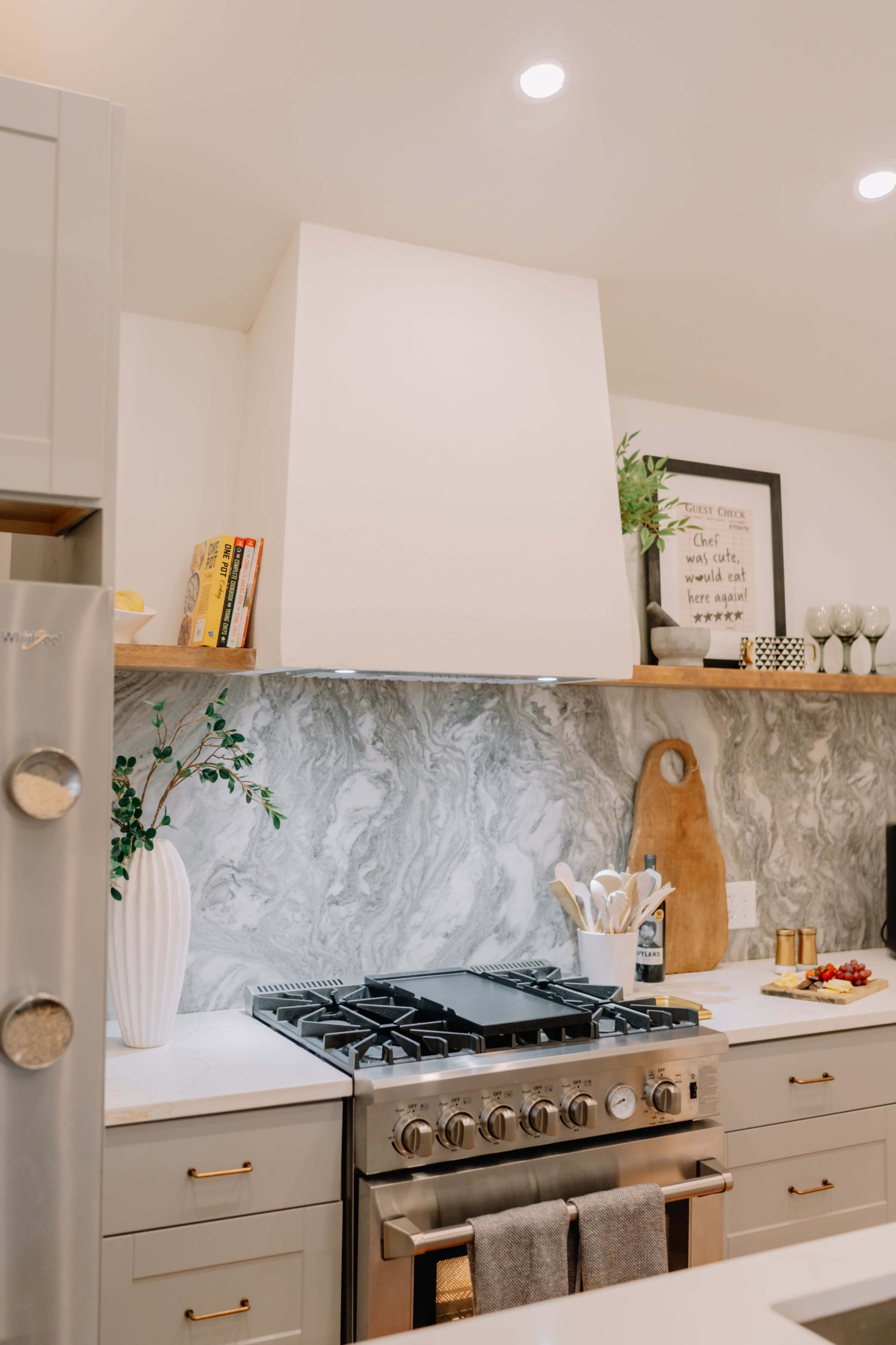 The kitchen features a modern stove with a marble backsplash, open shelving, and decorative items arranged on the countertop.