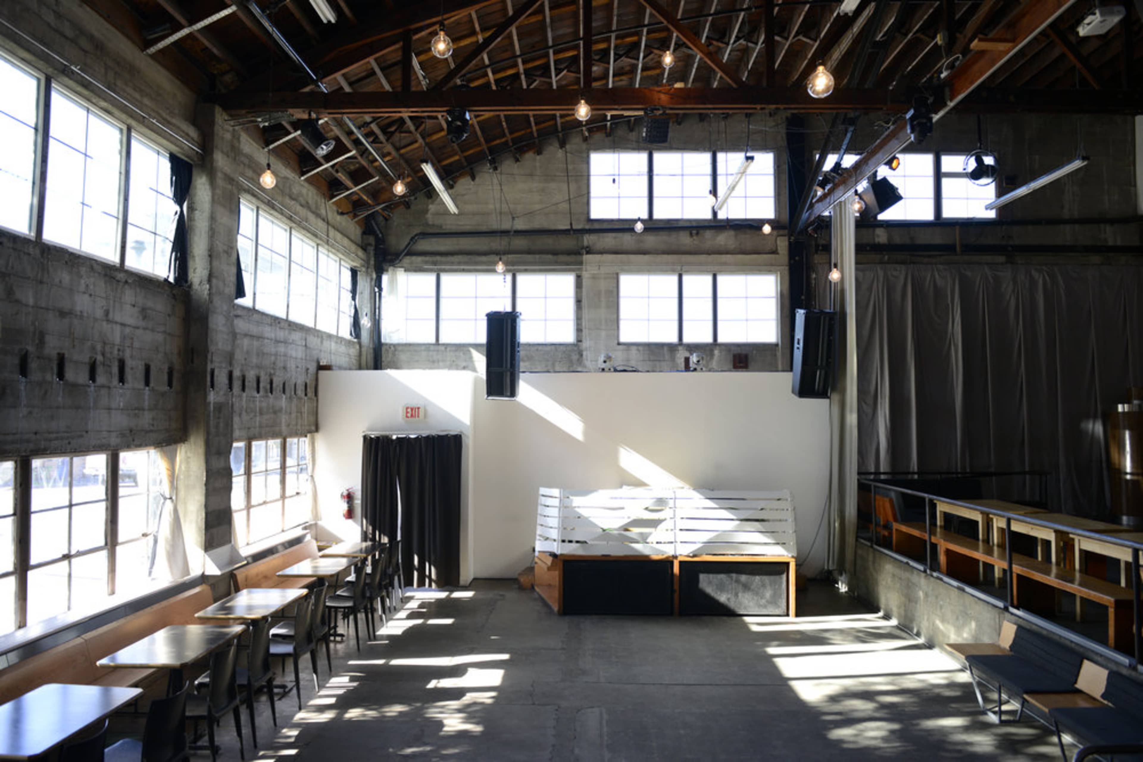 The interior of a spacious venue with large windows, exposed wooden beams, and a stage area at one end.