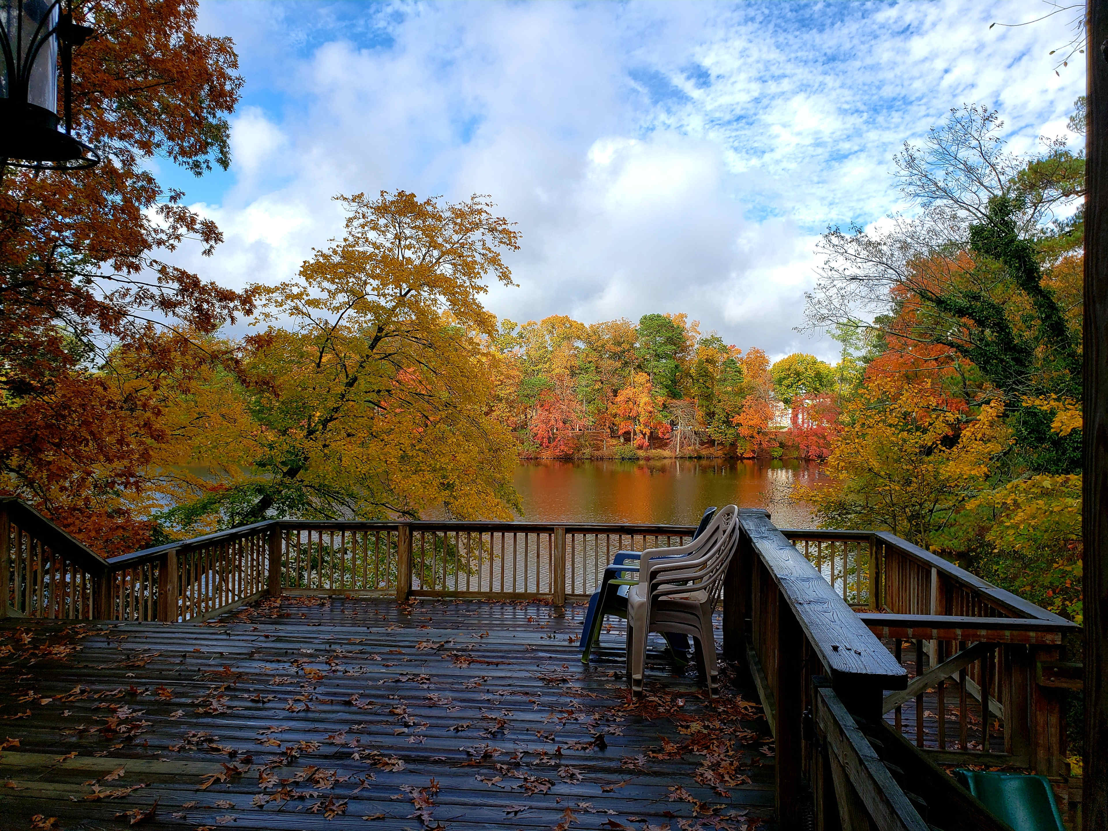 A wooden deck overlooks a lake surrounded by trees displaying autumn foliage.