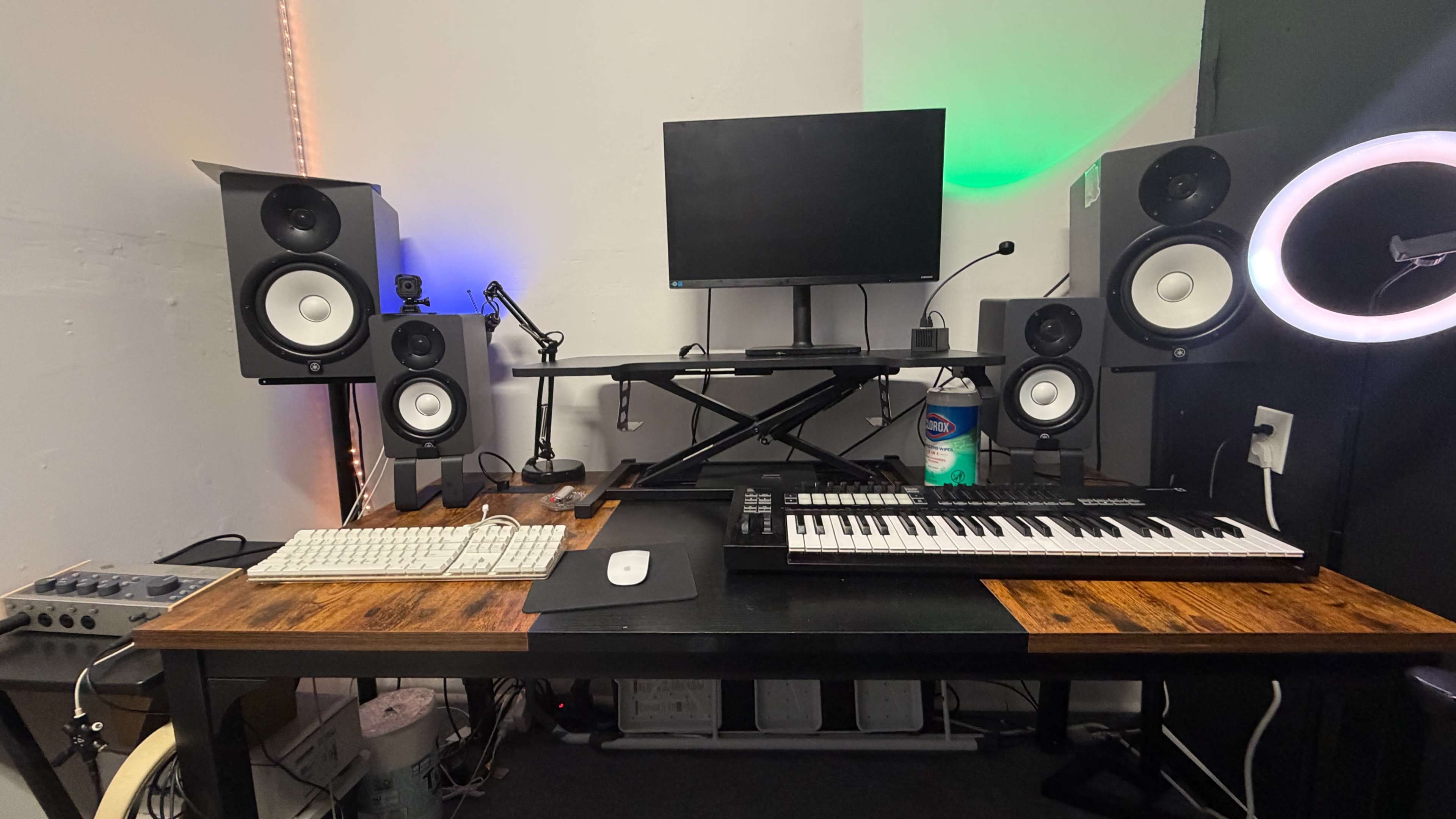 The image shows a home music production setup with a keyboard, computer monitor, studio monitors, and a clean wooden desk.