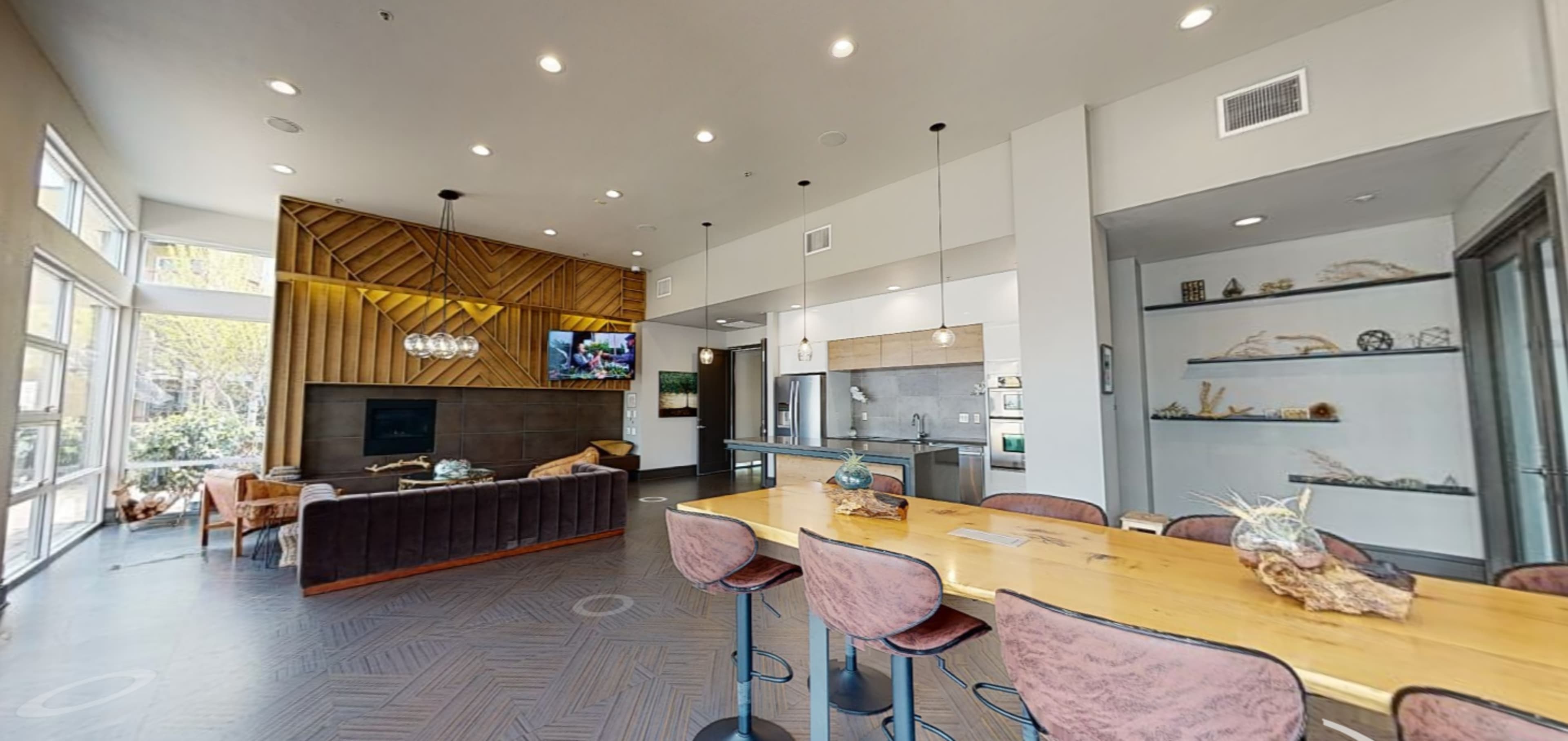 A modern communal lounge features a seating area with a couch, a dining table, and a kitchen area with sleek appliances.
