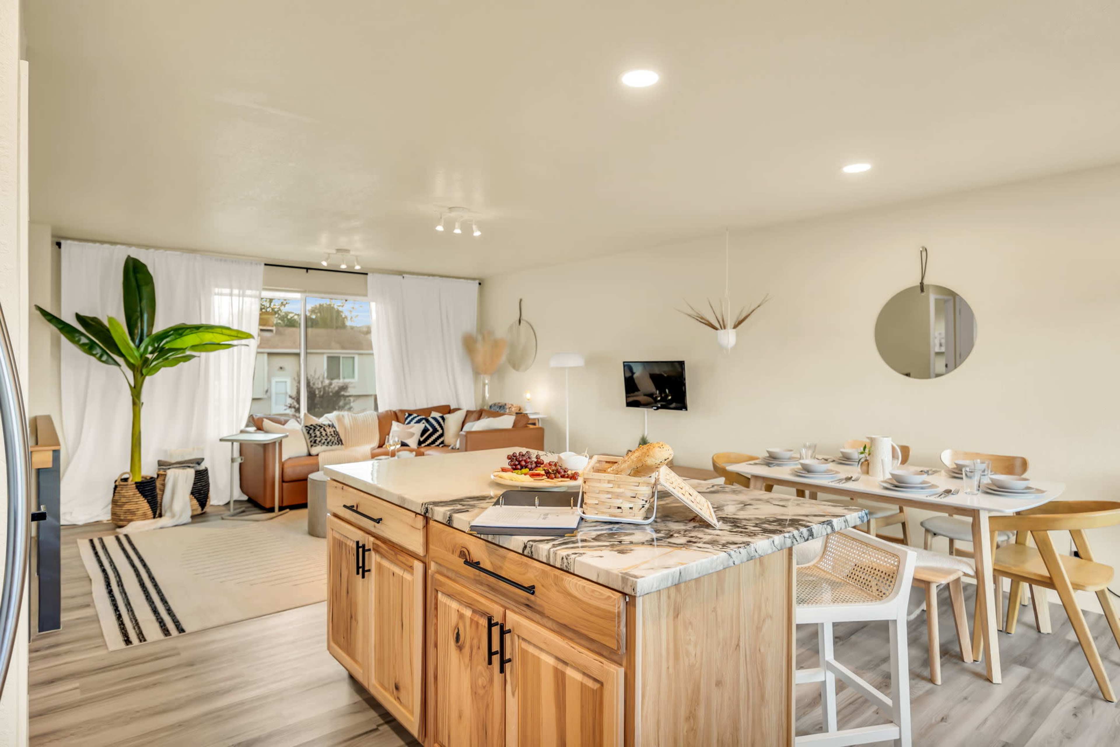 A modern living space features a kitchen island, dining area, and a seating area with a large window.