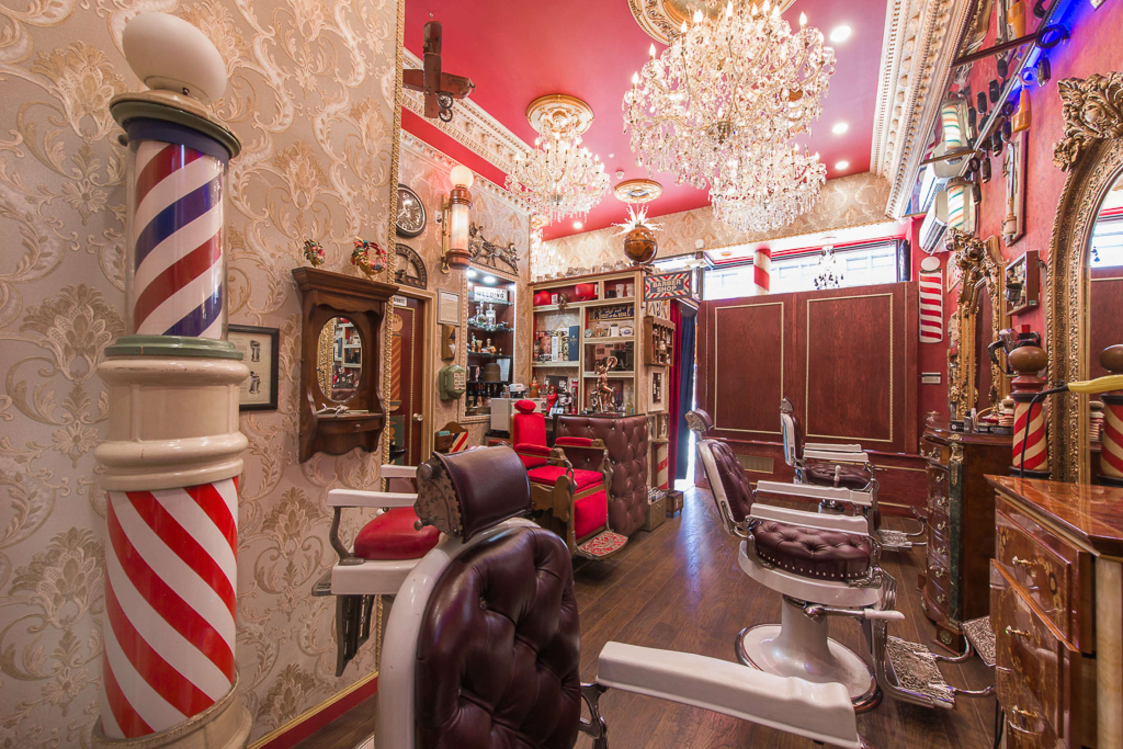 A vintage barber shop interior featuring red and white striped barber poles, ornate chandeliers, and classic leather barber chairs.