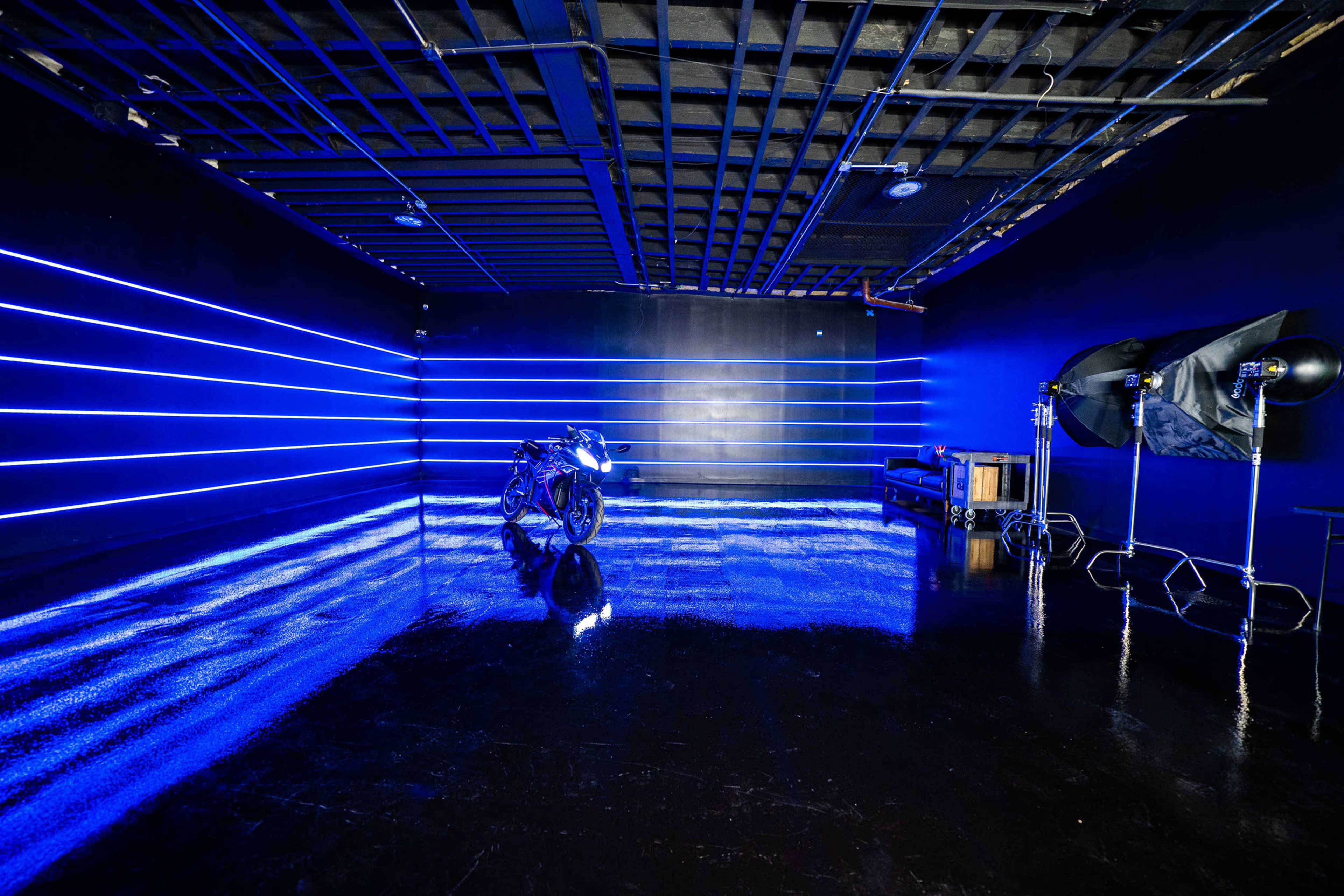 A dark studio space illuminated with blue LED lights, featuring a motorcycle positioned on a reflective surface.
