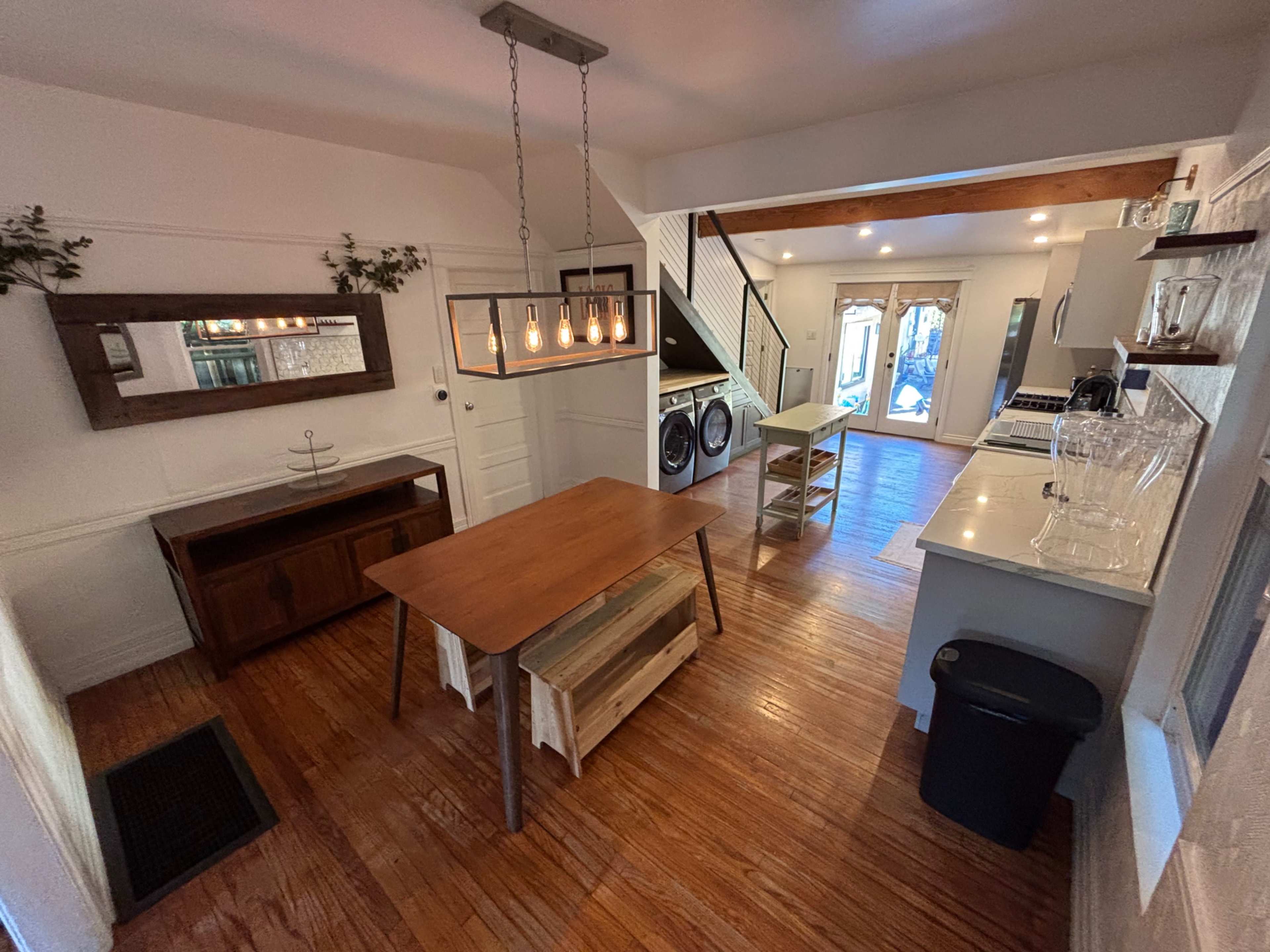 The image shows a spacious kitchen with wooden flooring, a central dining table, and a laundry area at the back, featuring modern appliances.
