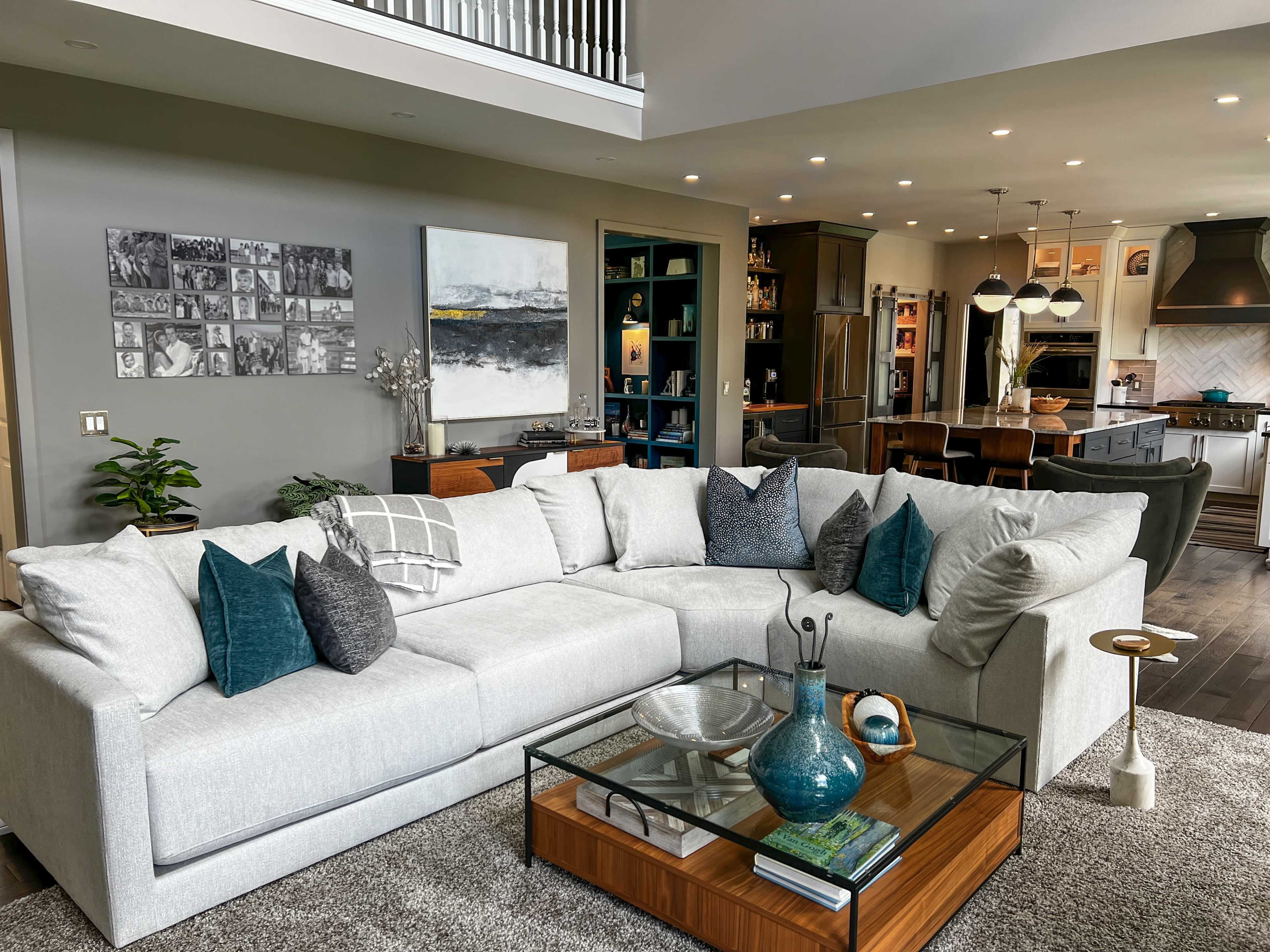 A modern living room with a large sectional sofa, a glass-top coffee table, and an open kitchen in the background.