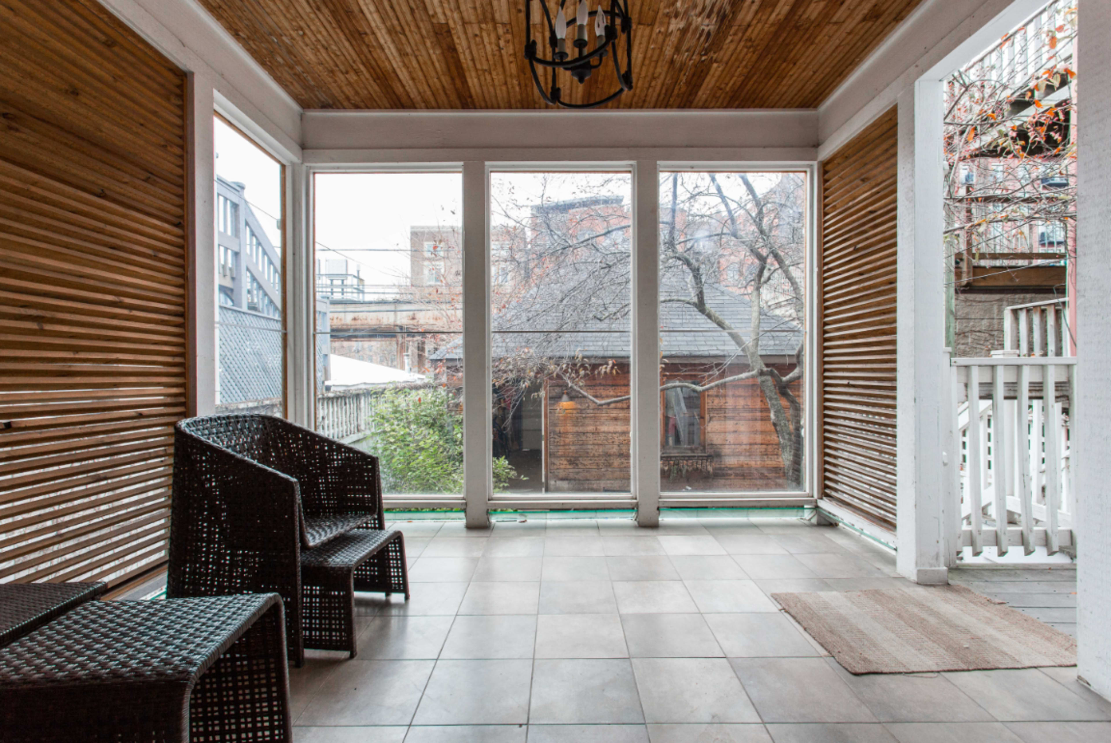 A screened-in porch features two wicker chairs and large windows overlooking a backyard with bare trees.