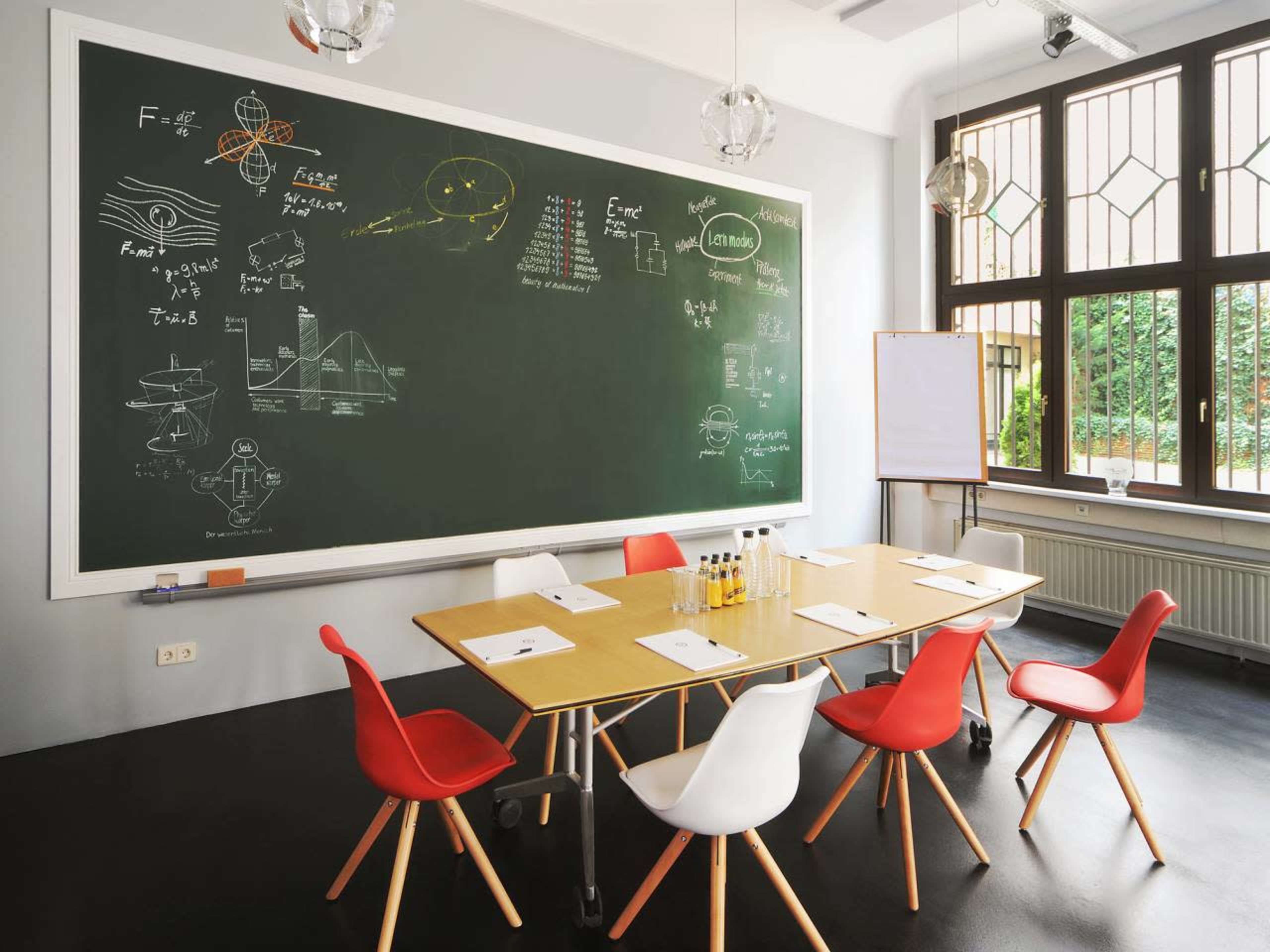 A conference room features a large chalkboard filled with scientific diagrams and equations, surrounded by a wooden table and colorful chairs.