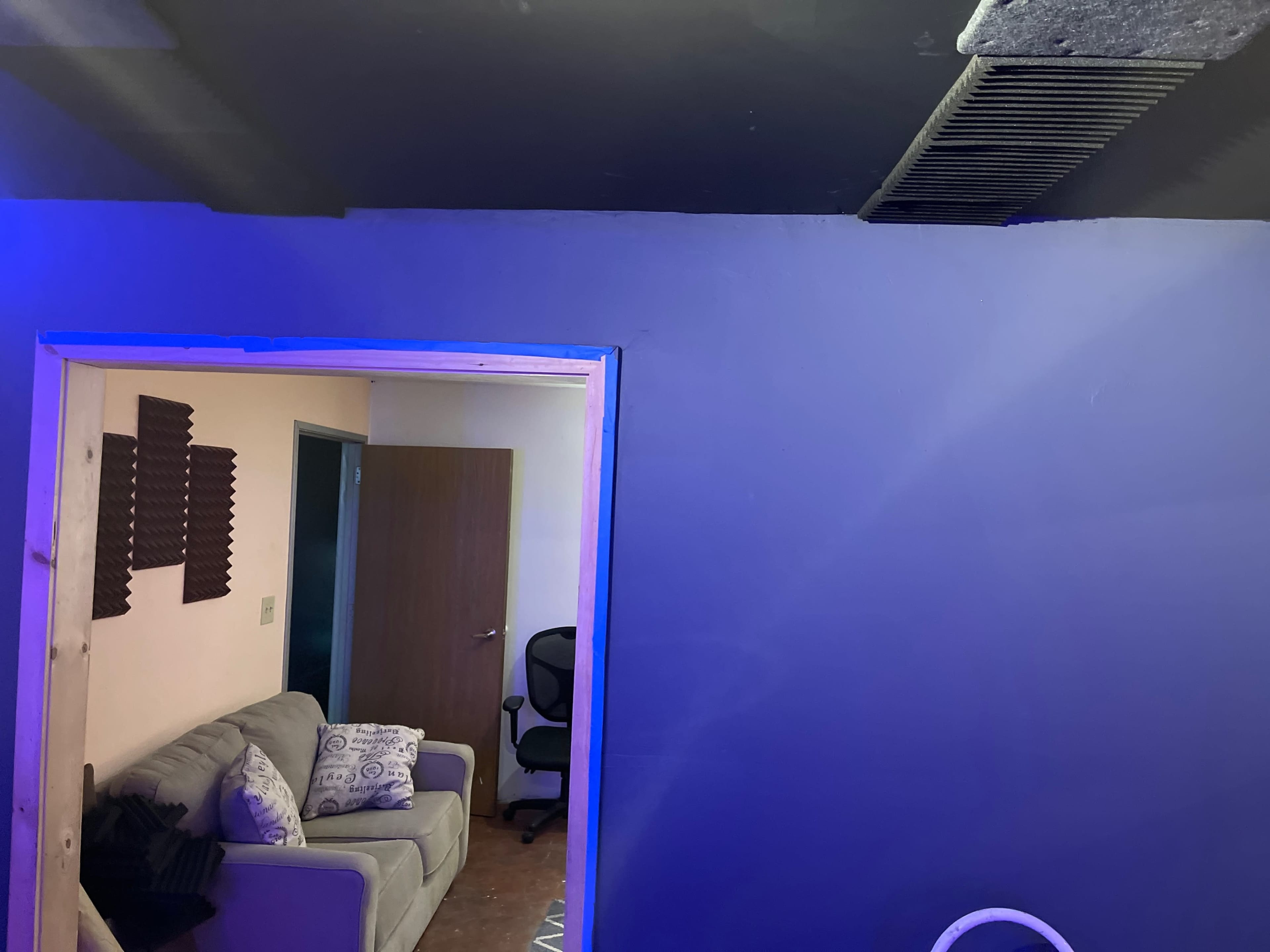 A room with a blue wall, a couch with decorative pillows, and an office chair visible through an open doorway.