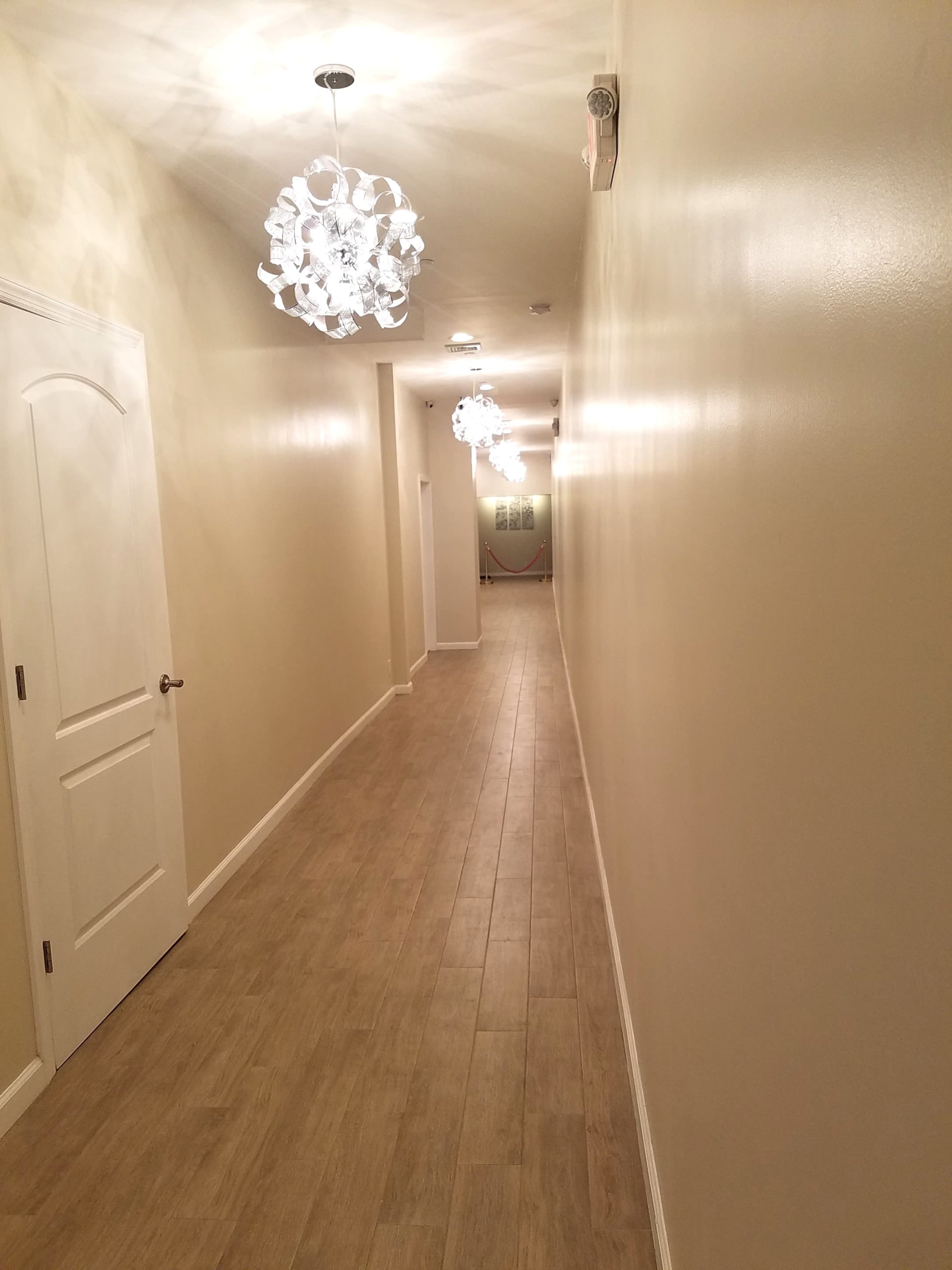 A long, well-lit hallway features light-colored walls and pendant lights hanging from the ceiling.