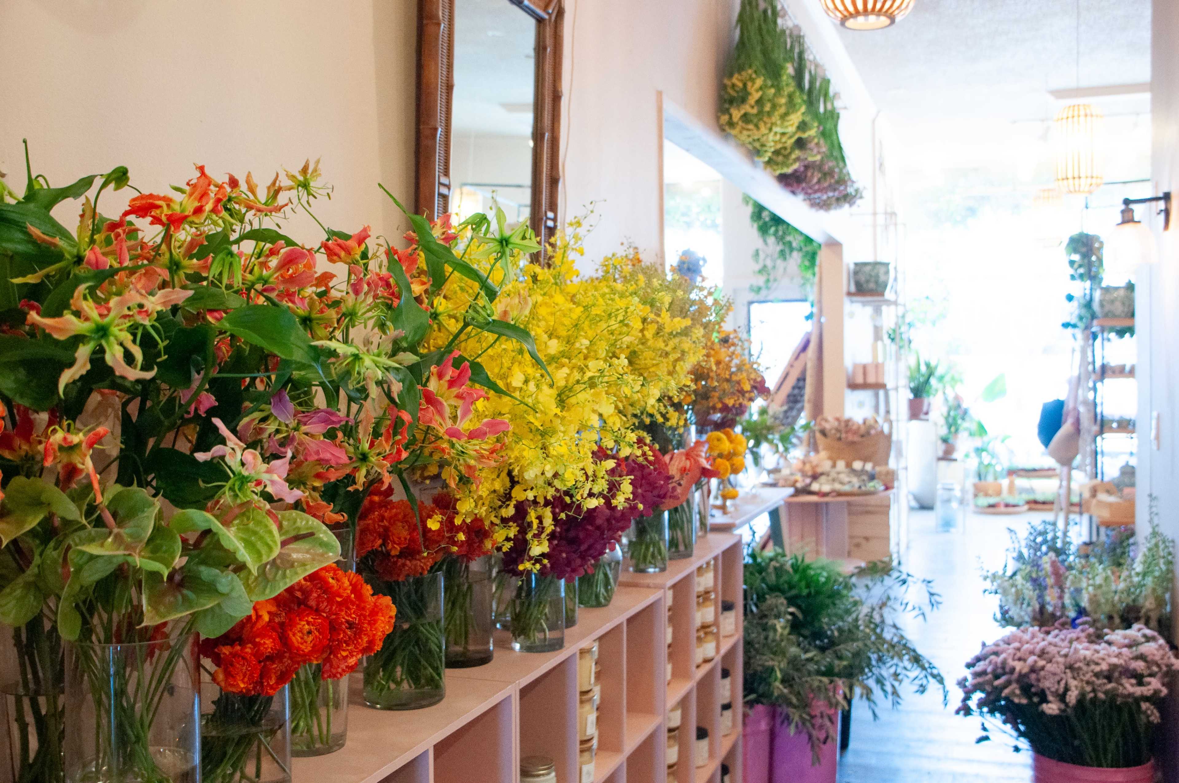 A flower shop displays a variety of colorful floral arrangements in glass vases along a wooden shelf.