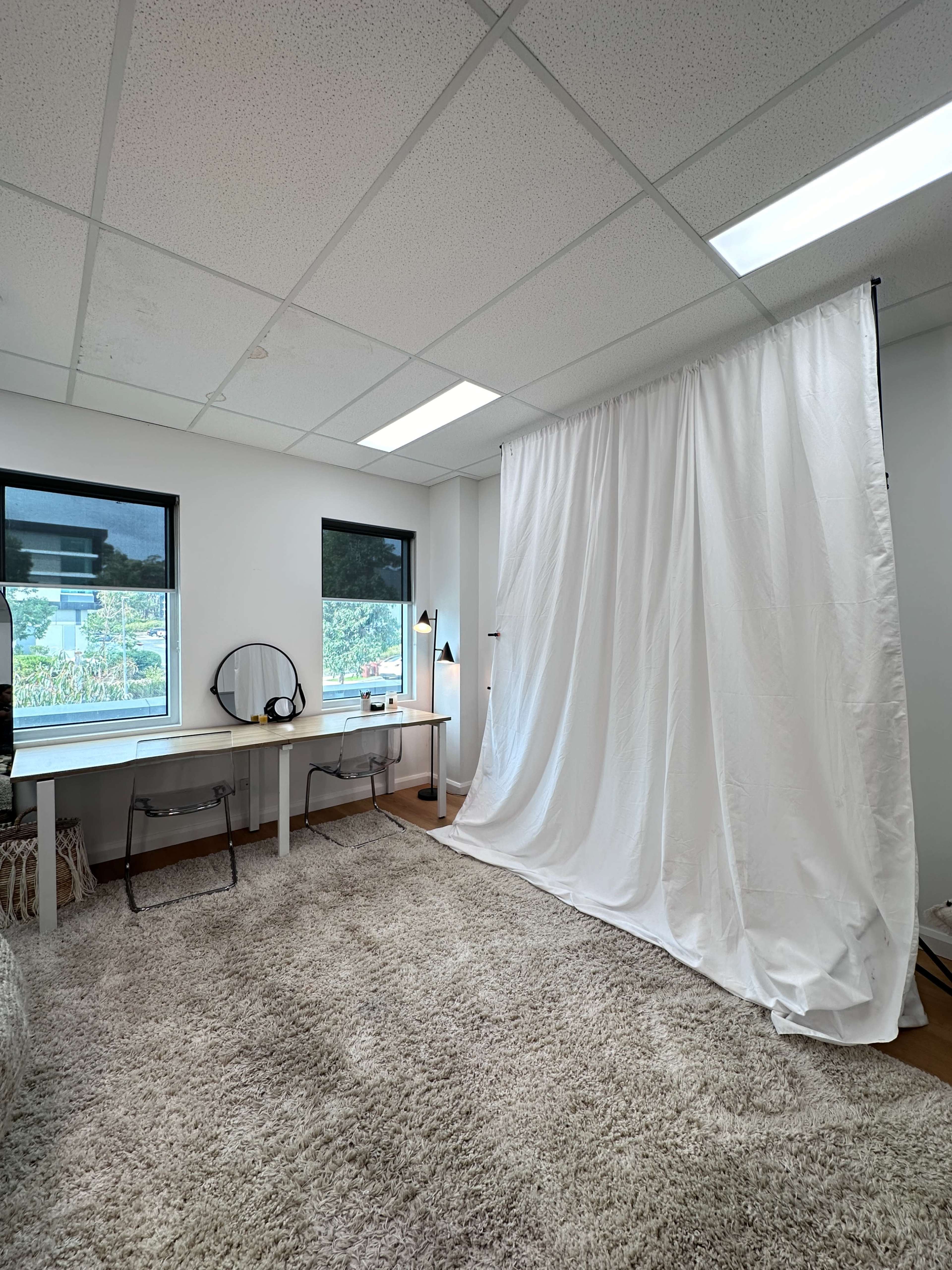 The image shows a bright room with a white backdrop, a table with a mirror, and a plush beige carpet.