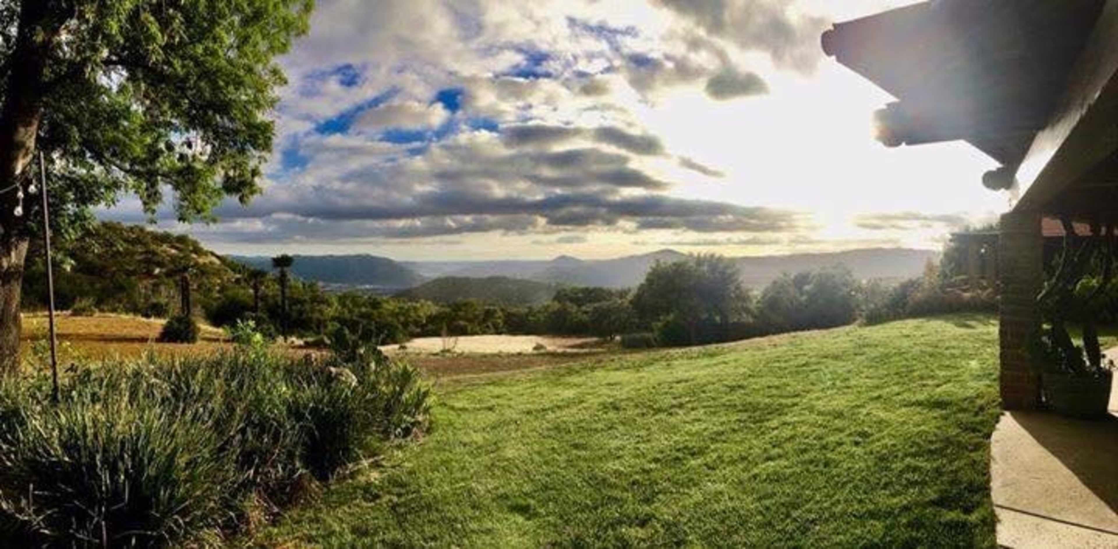 A panoramic view of rolling hills and valleys under a partly cloudy sky, with a well-manicured lawn in the foreground.