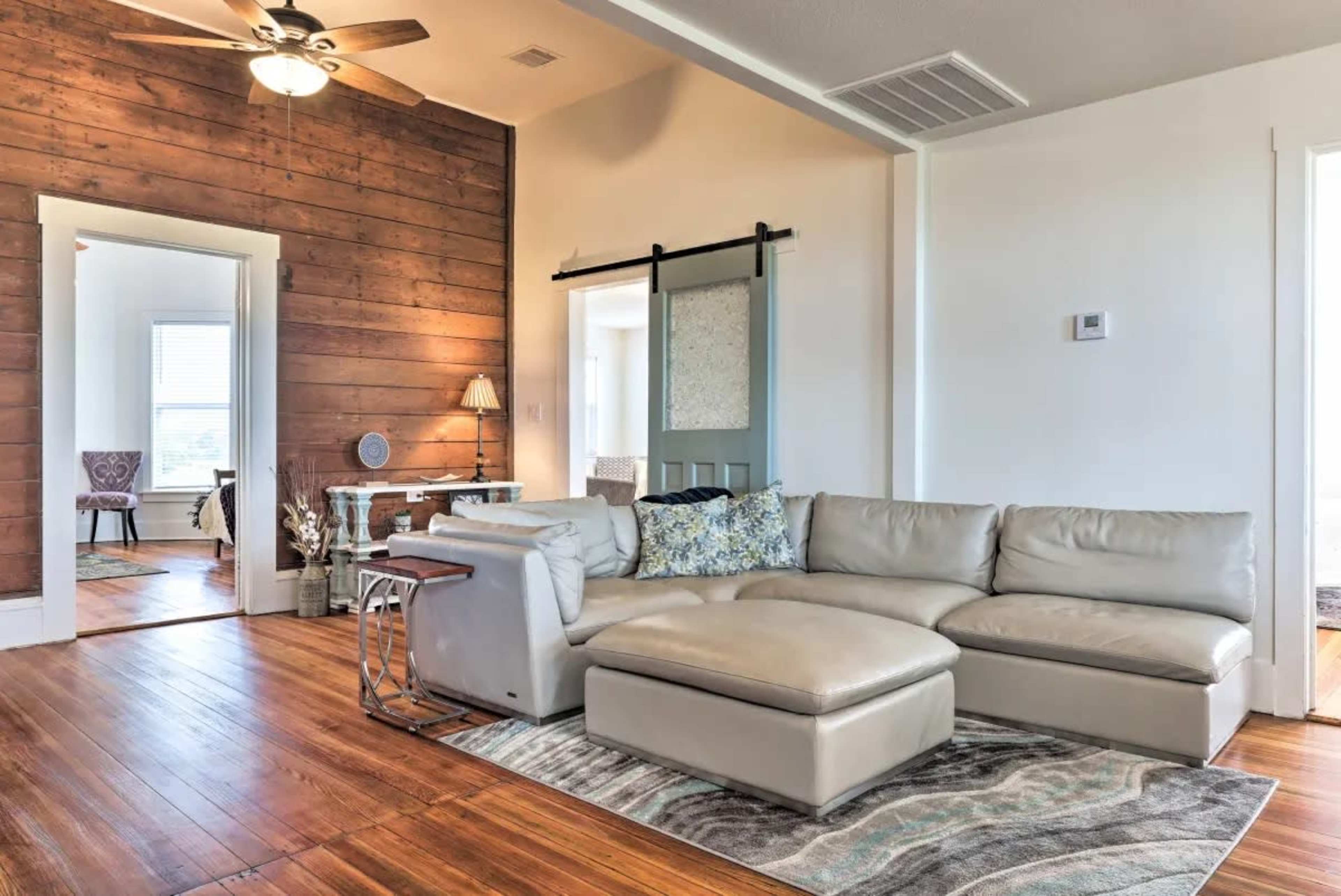 A modern living room featuring a light-colored leather sectional sofa, a wooden accent wall, and a sliding barn door.
