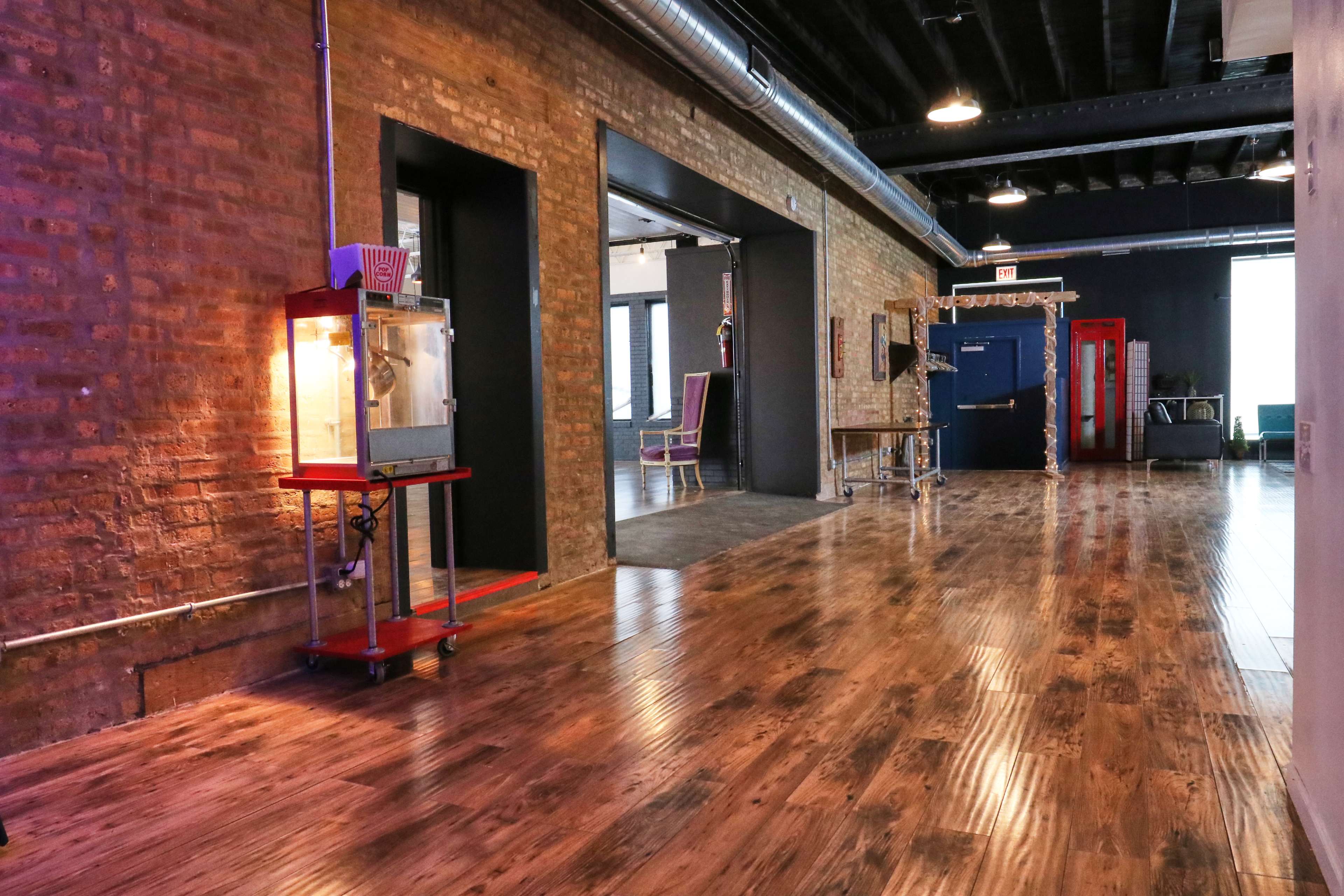 The image features a spacious interior with wooden flooring, exposed brick walls, and various doorways leading to different areas, including a popcorn machine on a cart.