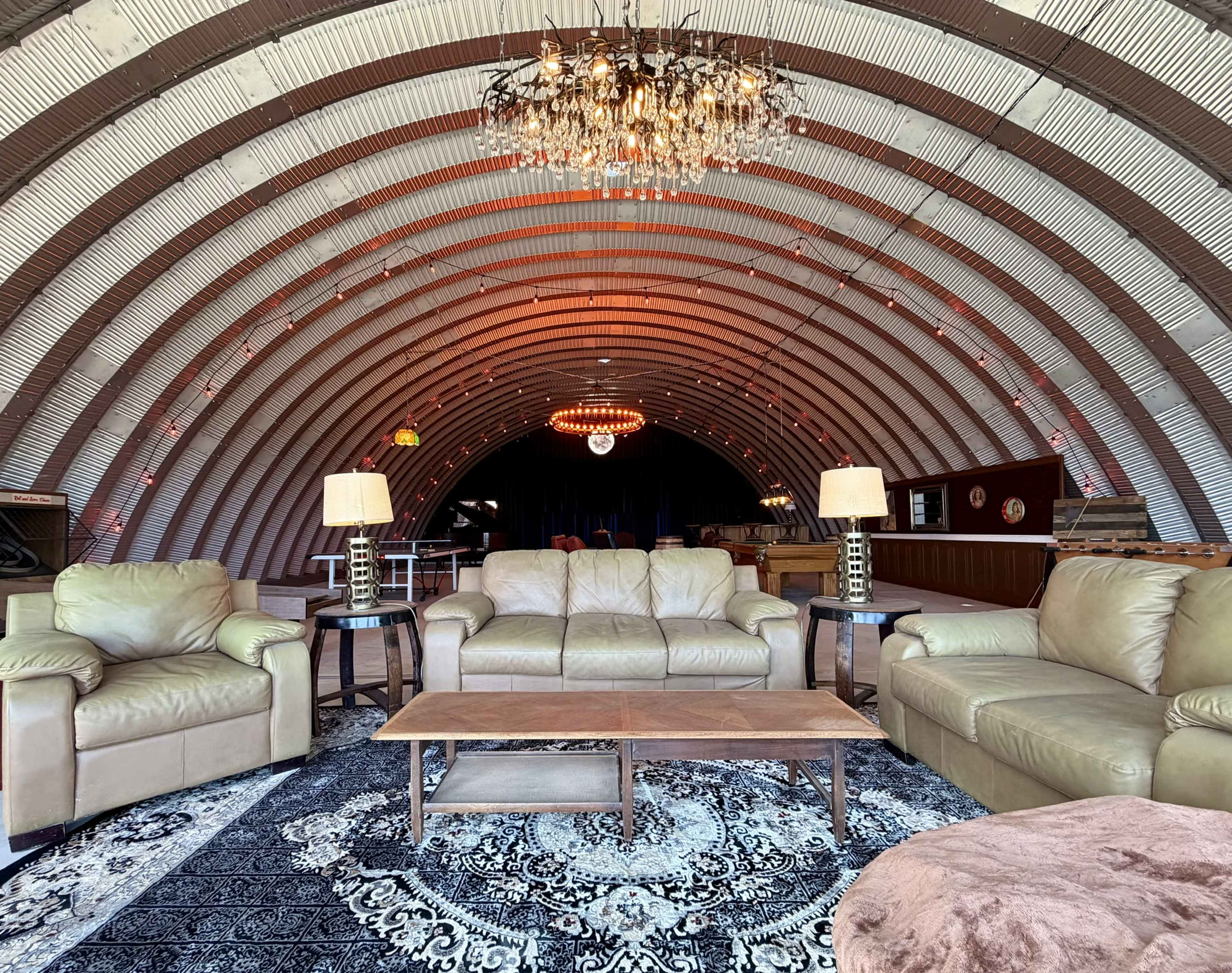 The interior of a spacious, curved building features a cozy seating area with leather sofas and a central coffee table, illuminated by a chandelier.