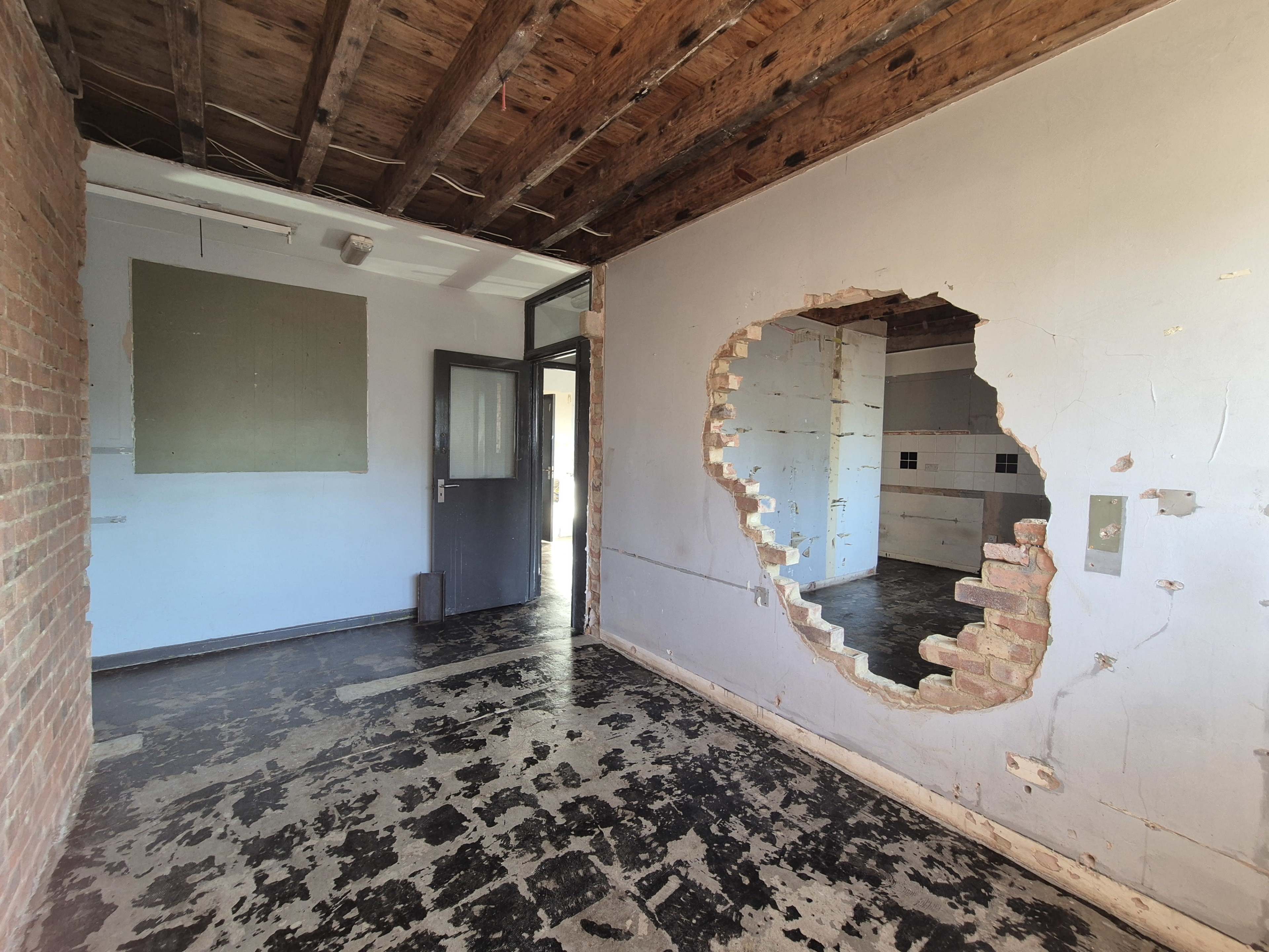 The image shows an interior room with exposed brick on one wall and a large hole cut through the wall, revealing another room behind it.