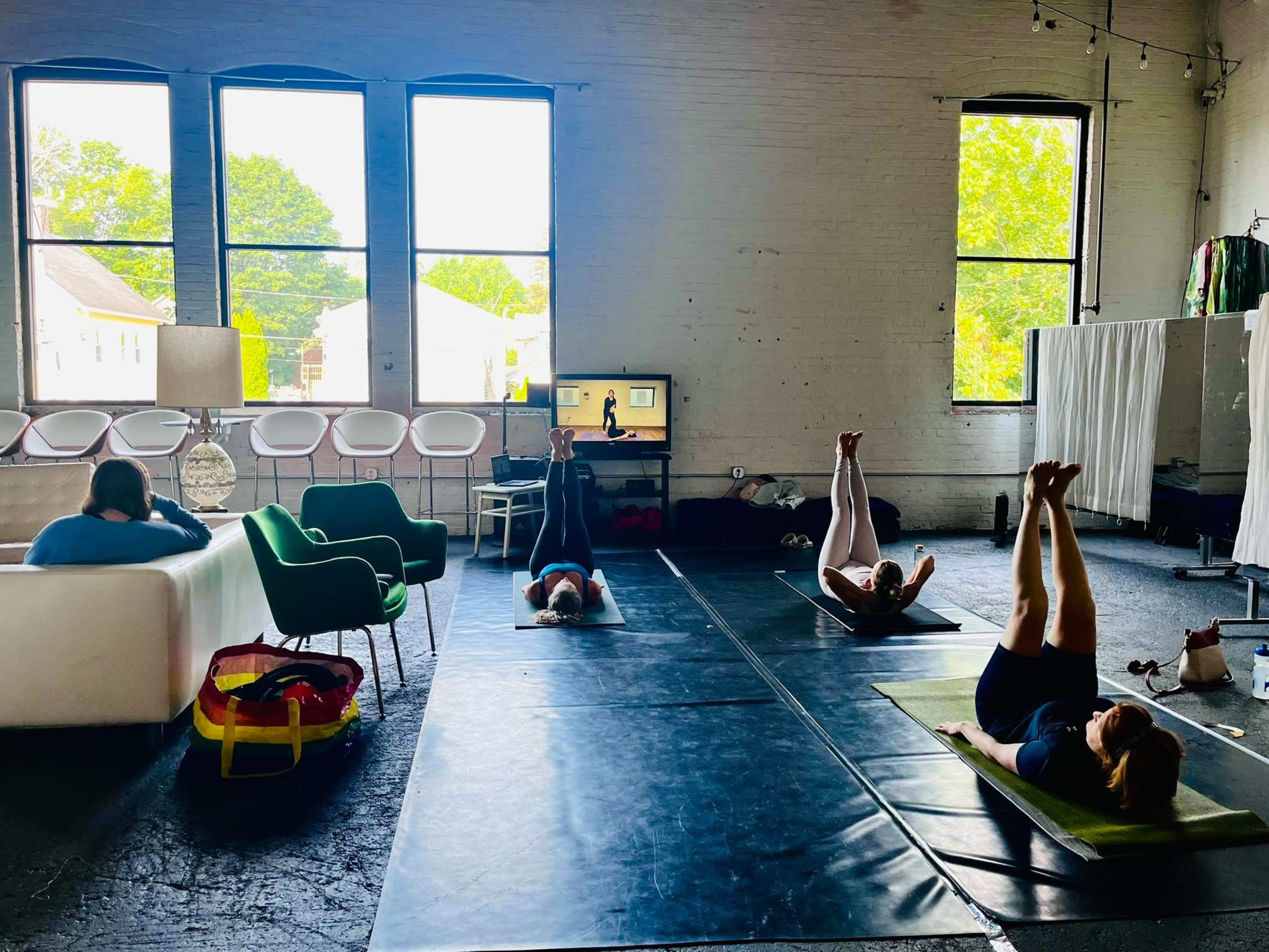 A small group of people is practicing yoga on mats in a spacious, well-lit room with large windows.