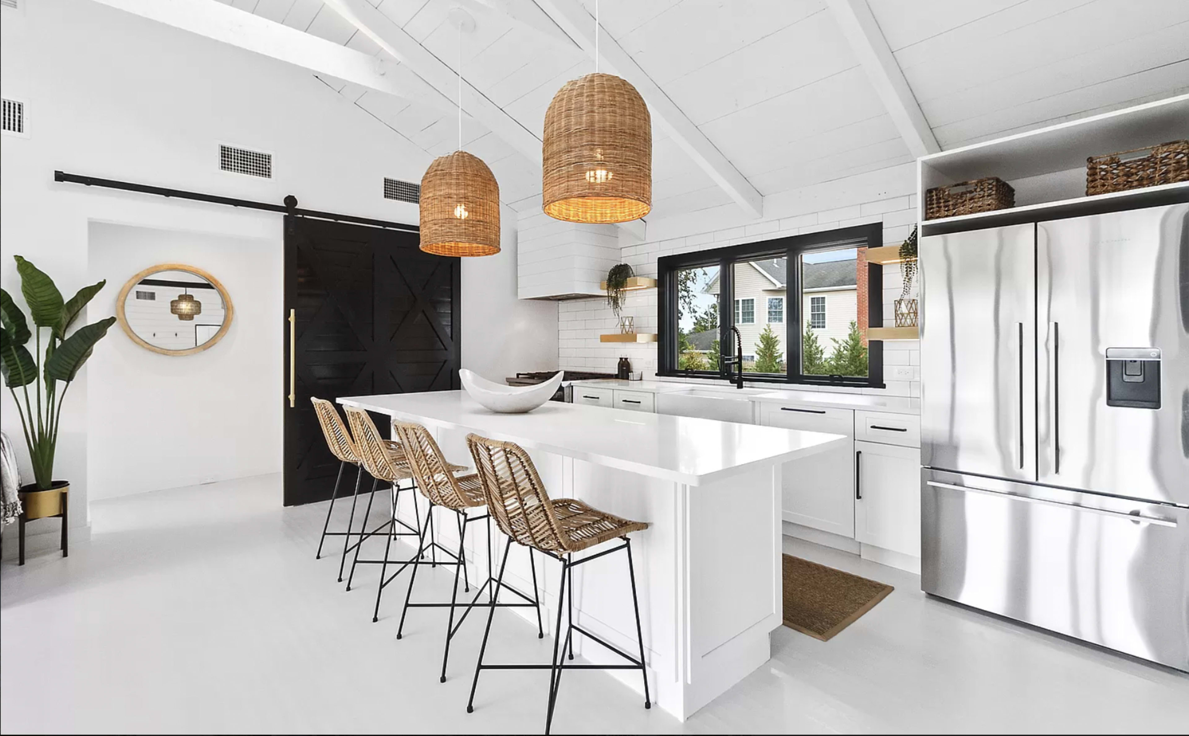 A modern kitchen features a white island with bar stools, pendant lighting, stainless steel appliances, and a sliding barn door.