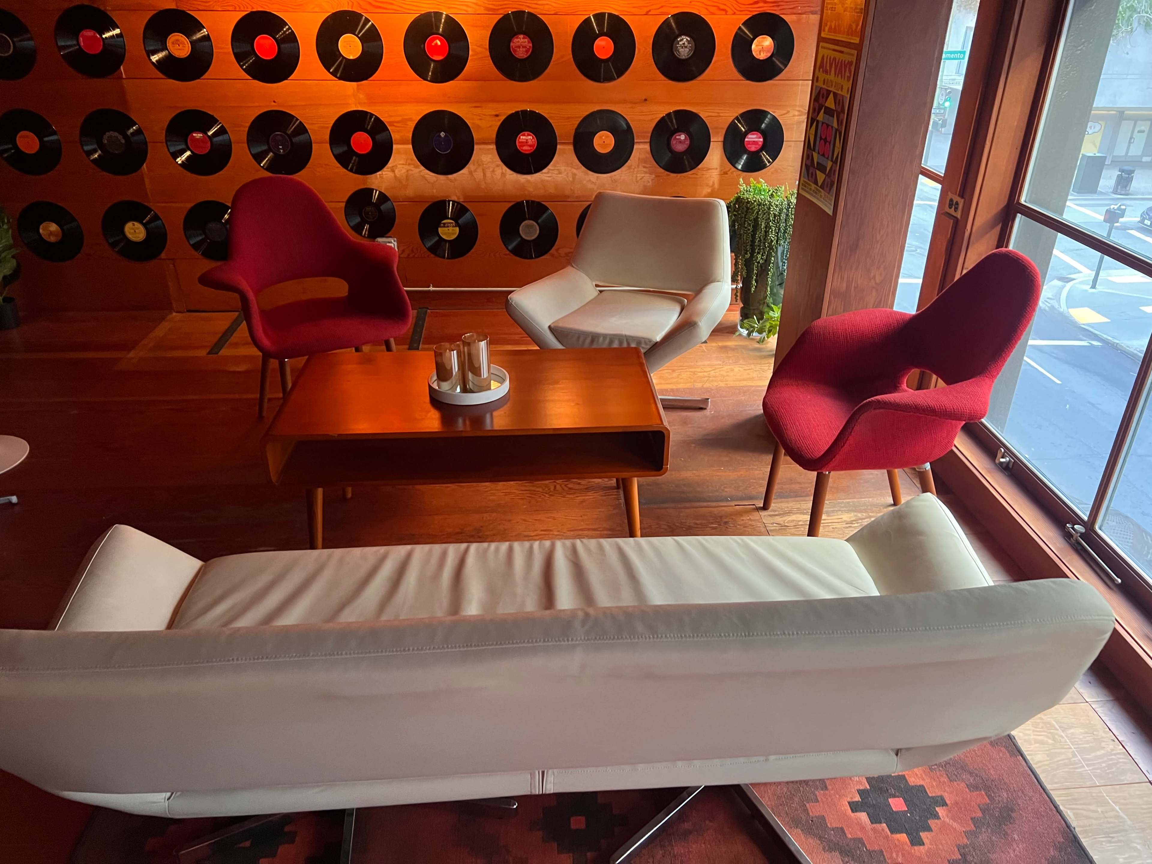 The scene features a cozy seating area with a white sofa and three colorful armchairs surrounding a wooden coffee table, set against a wall adorned with vinyl records.