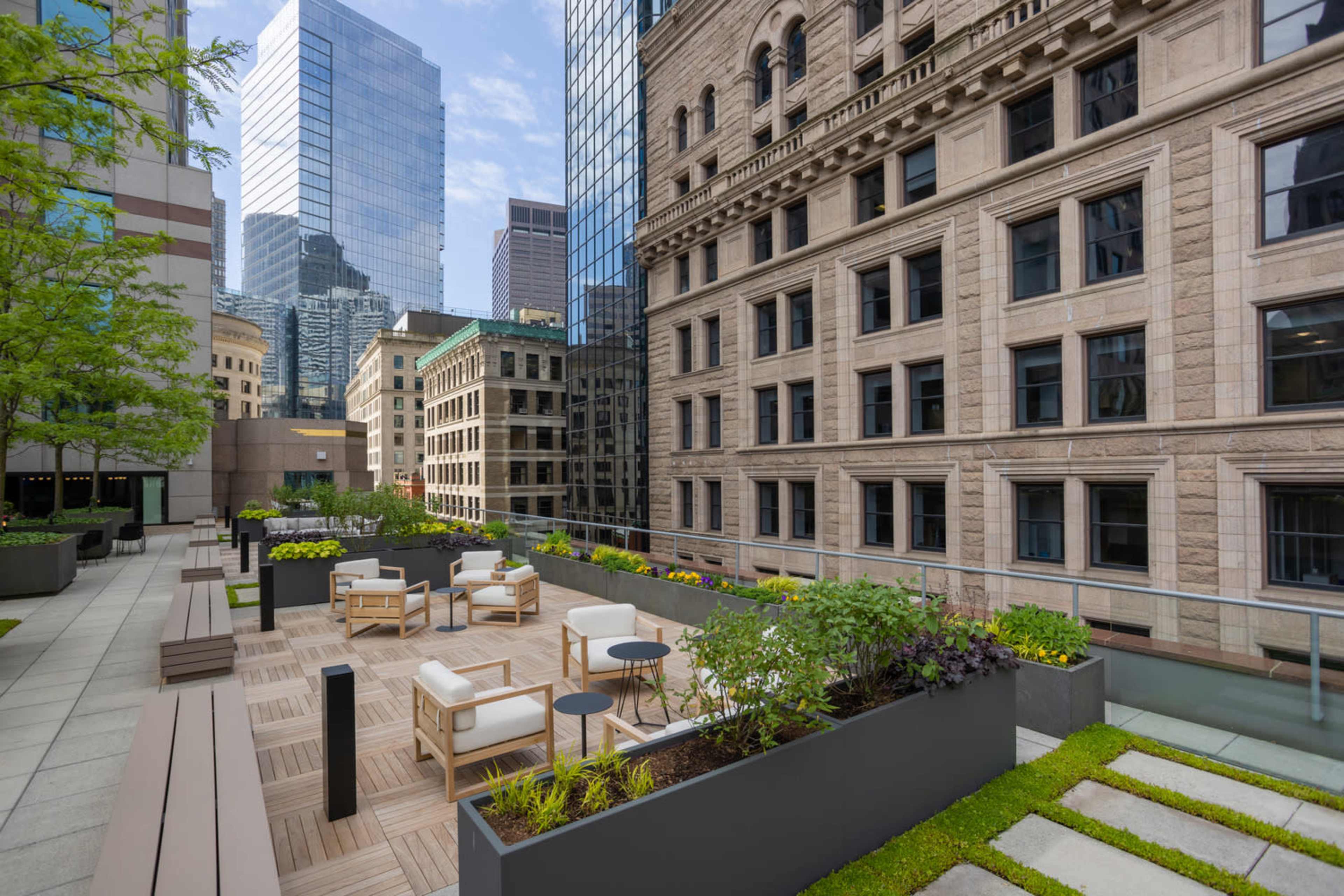 A rooftop garden with modern seating and planters, surrounded by tall buildings in an urban setting.