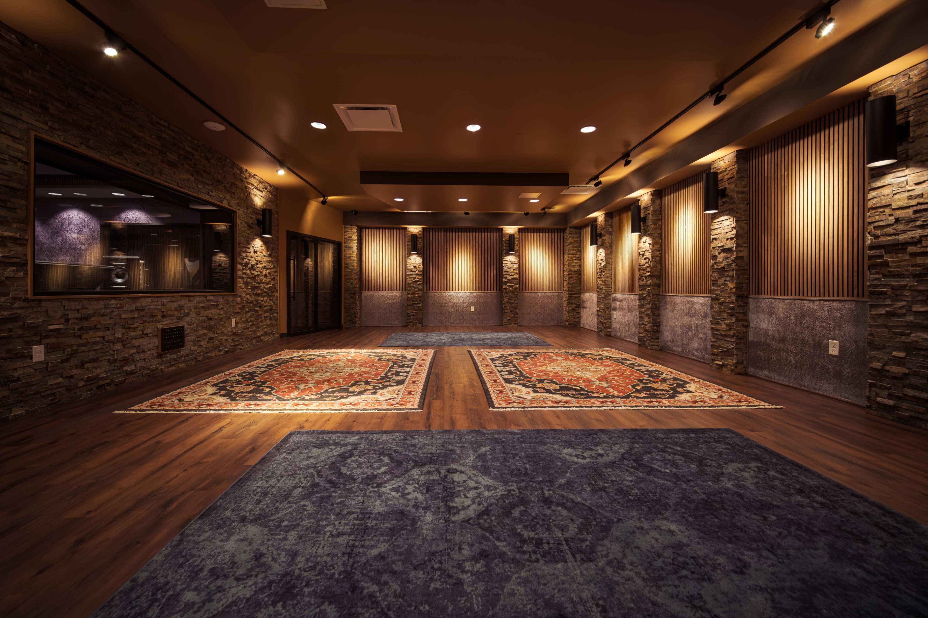 The image depicts a spacious interior room featuring decorative stone walls, wooden flooring, and ornate rugs on the ground.