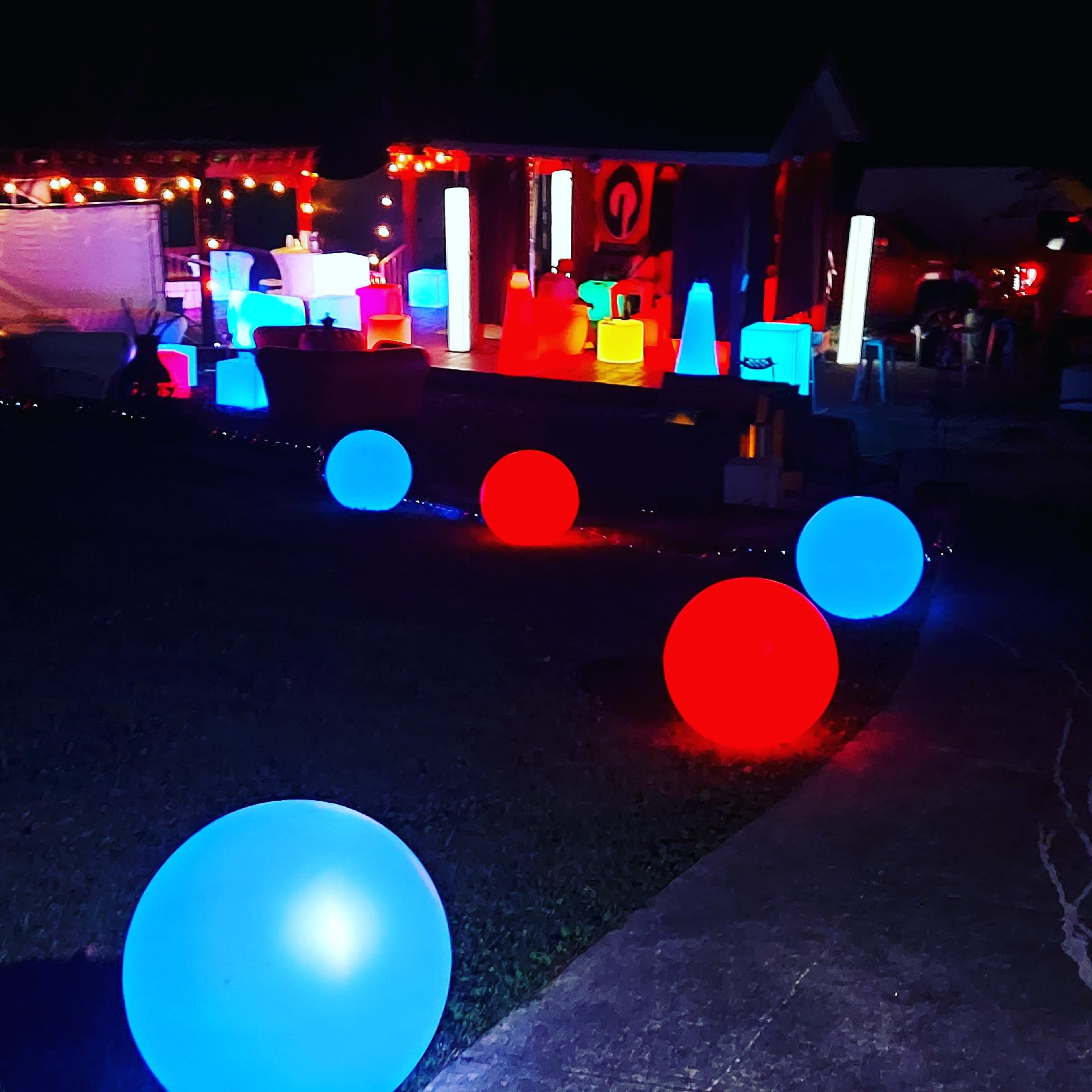 The scene features a decorative outdoor area illuminated by various colorful, glowing orbs and shapes, with blue and red lights highlighting a pathway and surrounding structures.