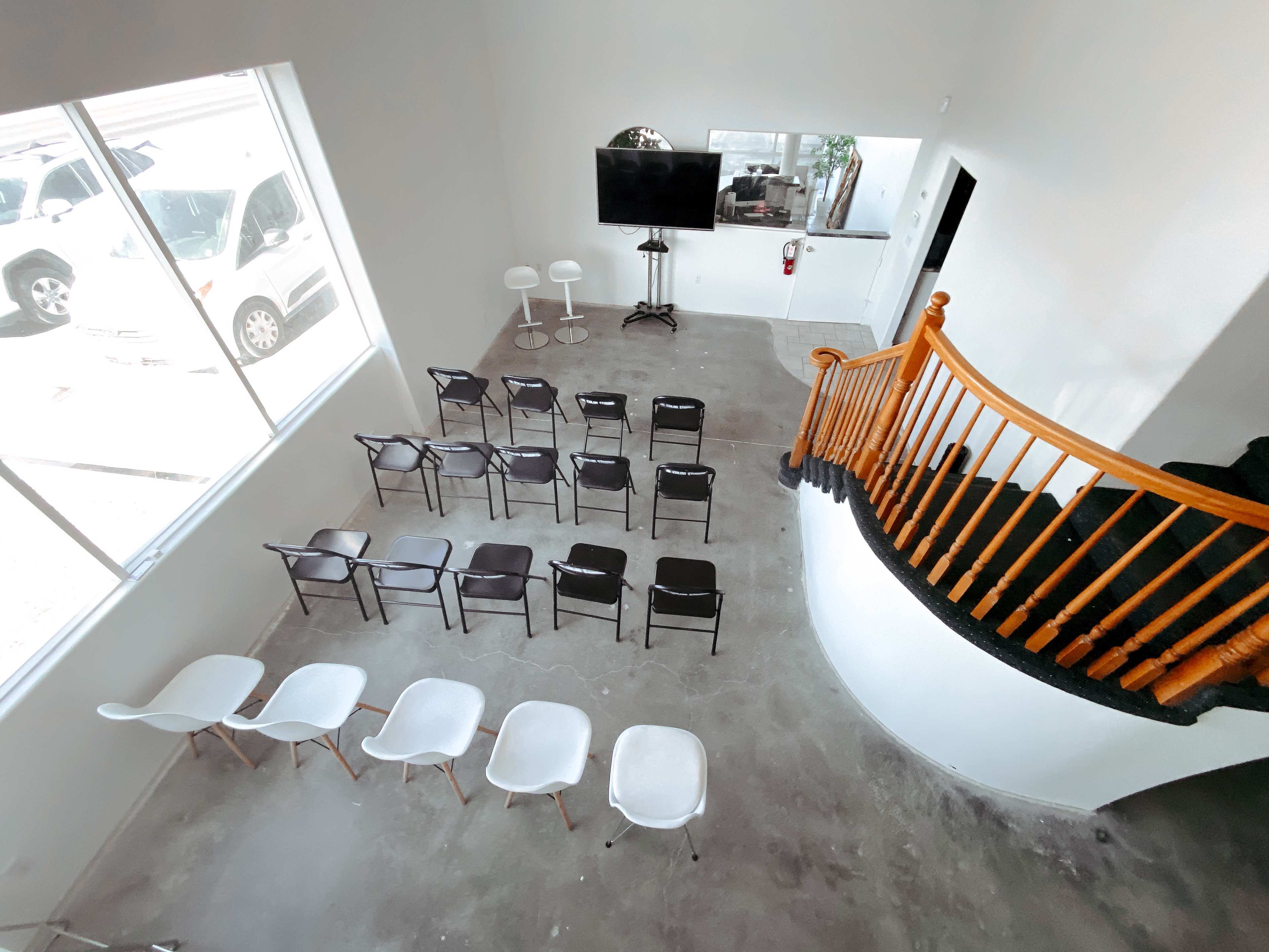 An interior space with a staircase on the right, arranged seating in rows on the floor, and a television screen mounted on the wall.