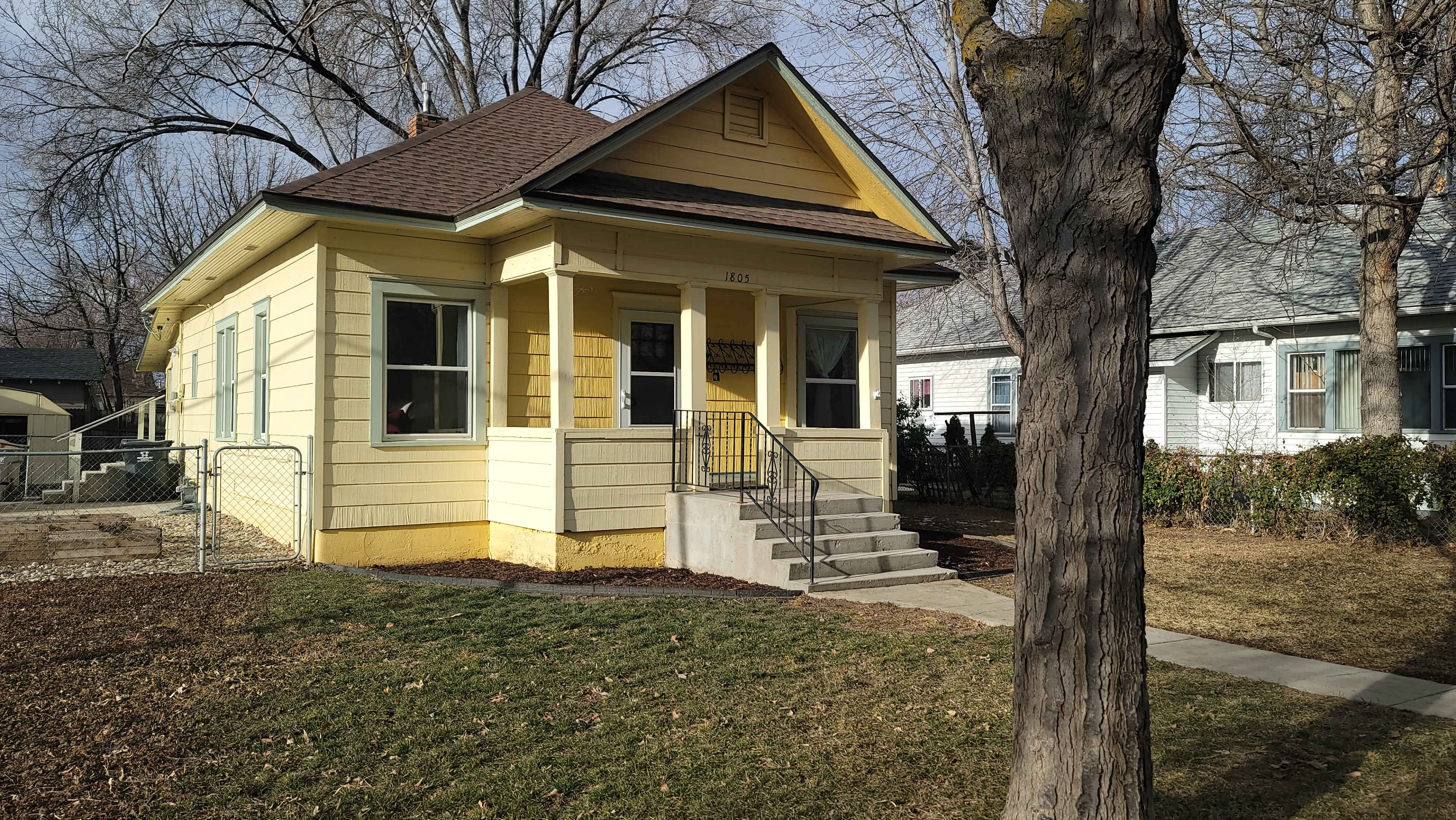 A yellow house with a porch and steps surrounded by trees and a lawn.