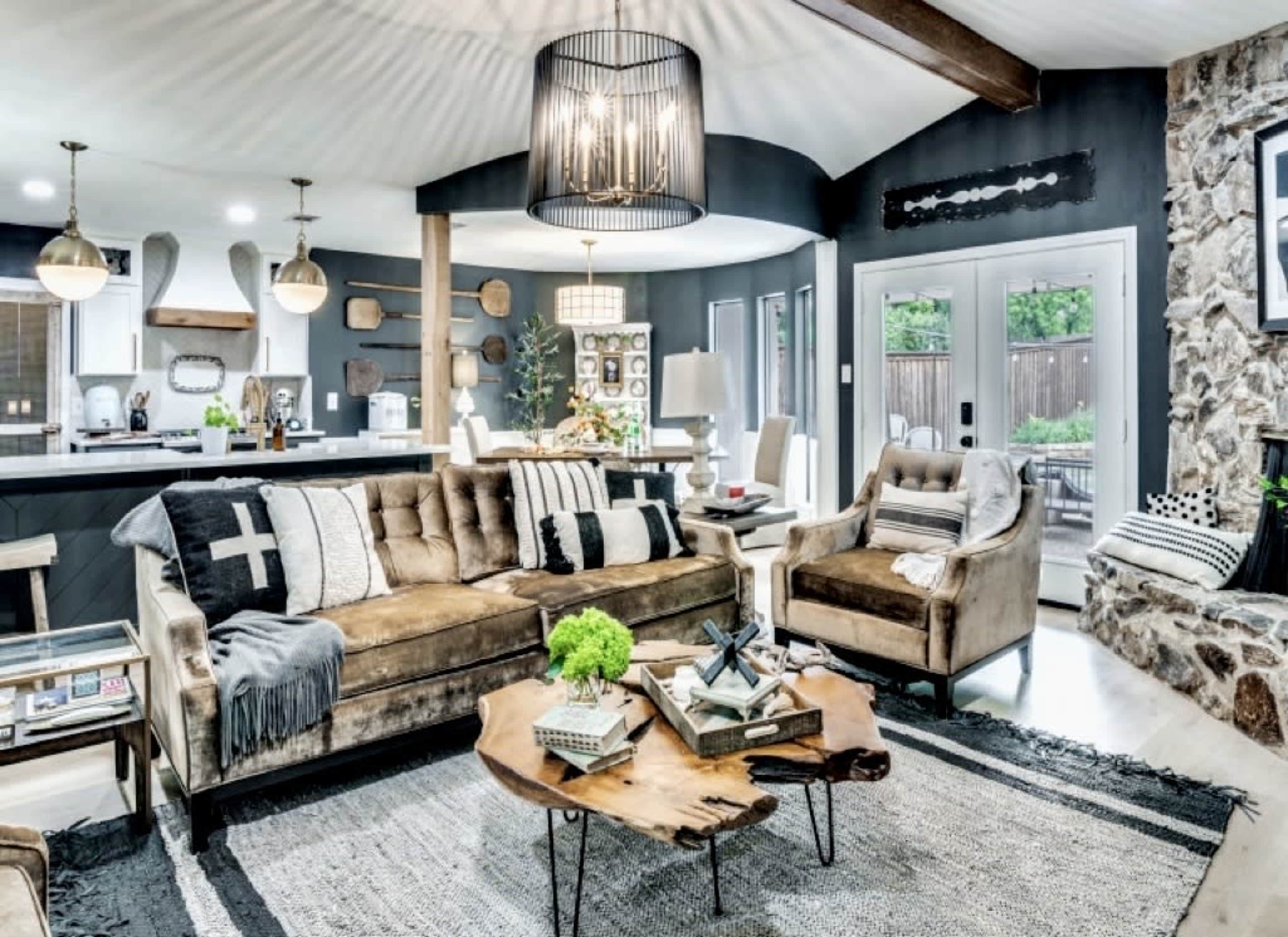 A modern living room features a plush brown sofa and armchair, a wooden coffee table, and a stone accent wall, with an open kitchen visible in the background.