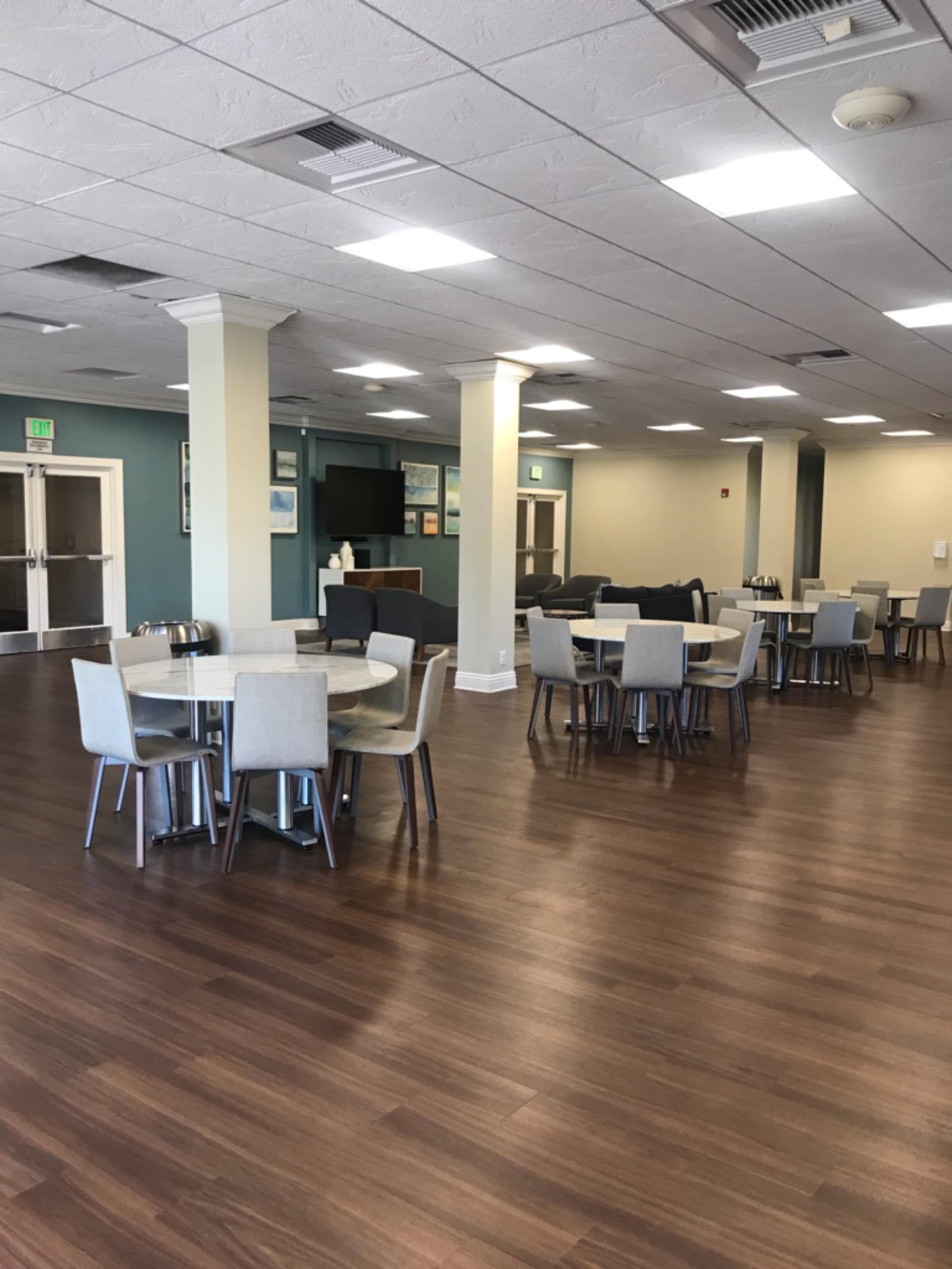 A spacious dining area with several tables and chairs arranged on a wooden floor, featuring blue and beige walls.