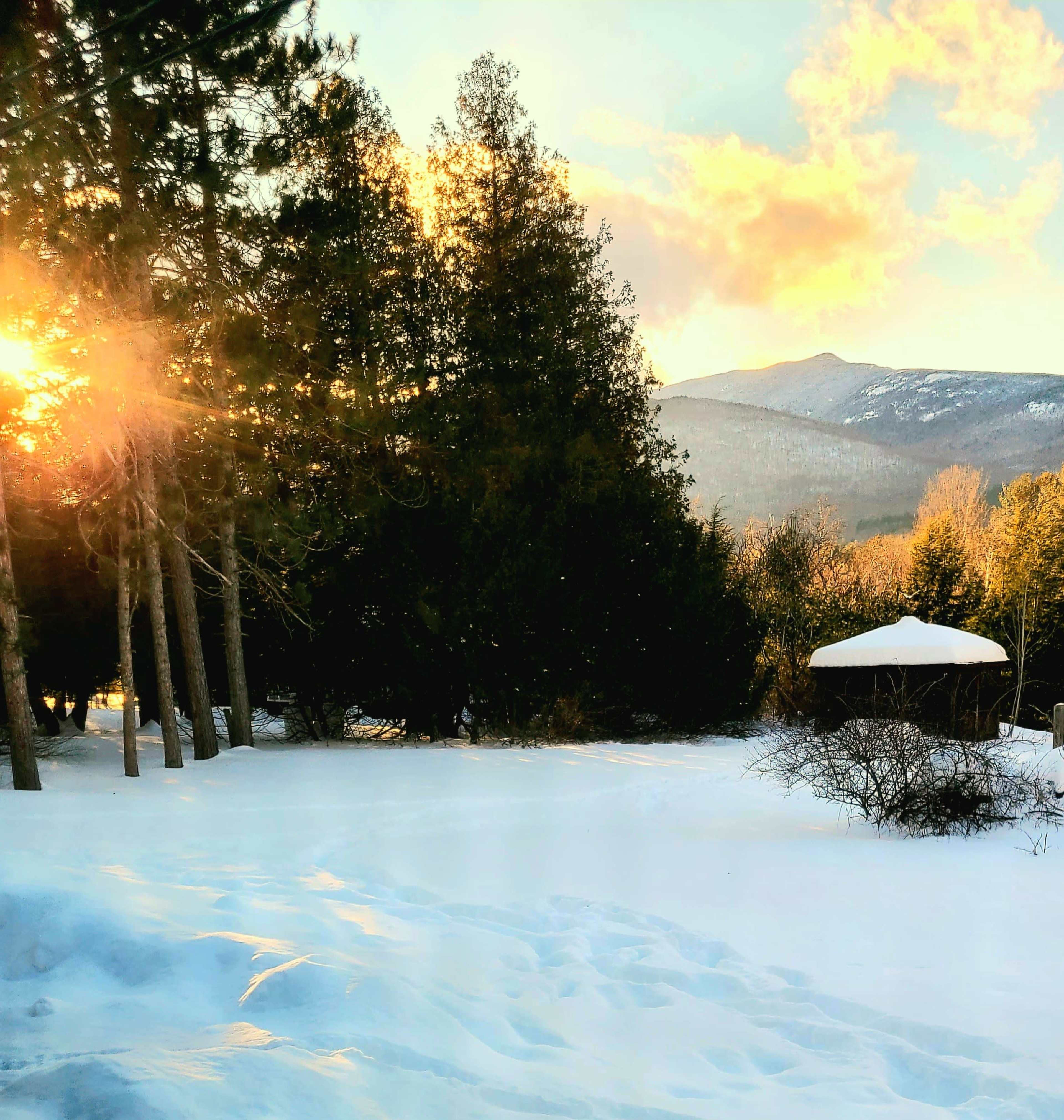 A snowy landscape with a circular structure and mountains in the background, illuminated by the warm light of the setting sun.