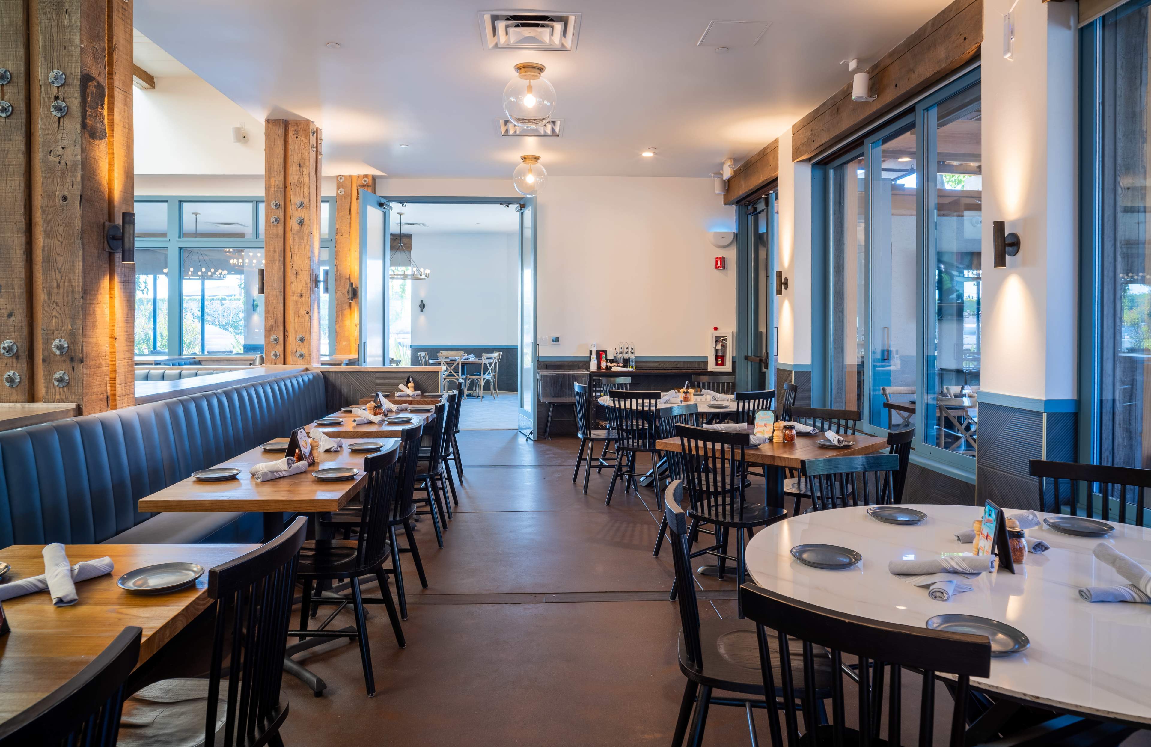 The image features a restaurant interior with wooden beams, tables set for dining, and a combination of blue booths and black chairs.